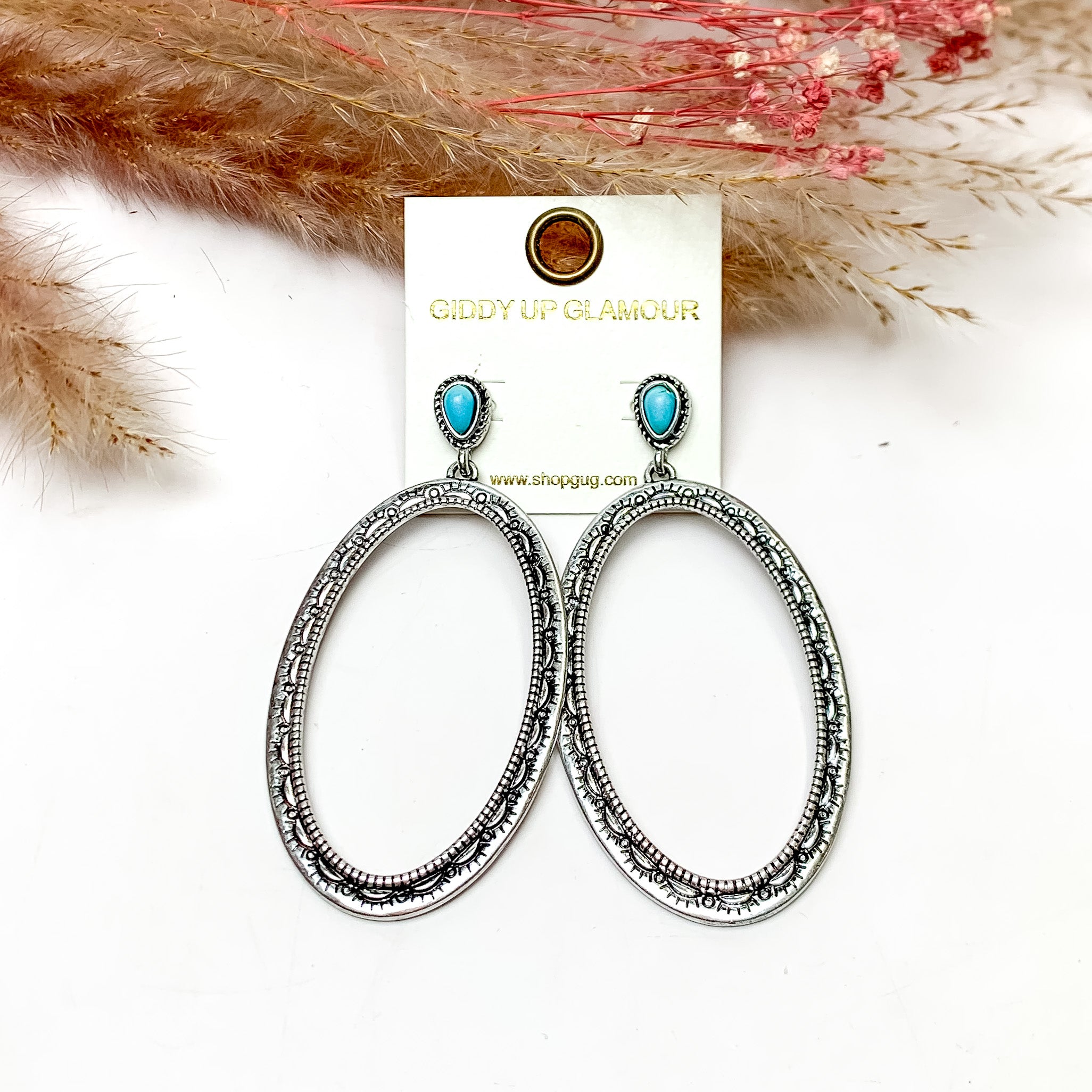 Oval Large Silver Tone Earrings With Turquoise Posts. These earrings are pictured on a white background with plants behind for decoration.