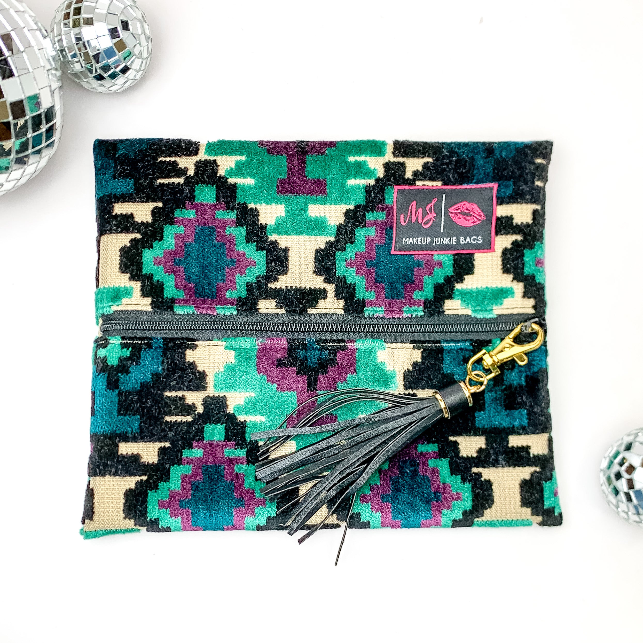 Pictured on a white background with disco balls at top is a mini lay flat bag in a midnight aztec print. This bag includes a middle zipper and a tassel.