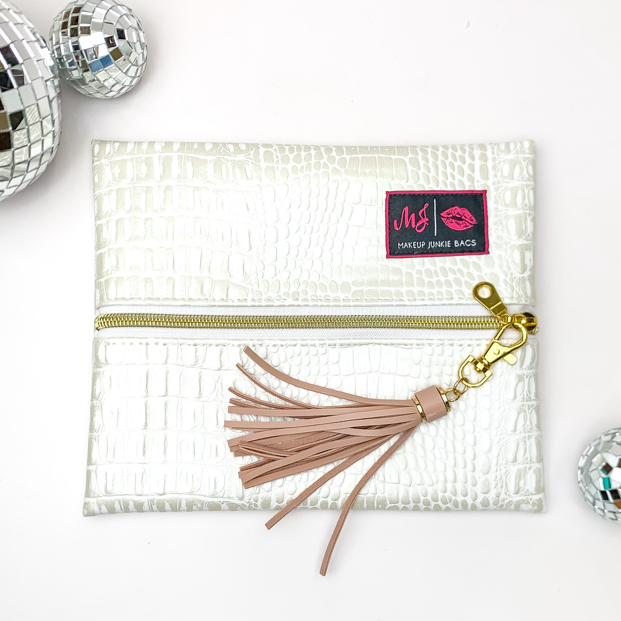 Pictured on a white background with disco balls at top is a mini lay flat bag in a pearl white gator print. This bag includes a middle zipper and a tassel.