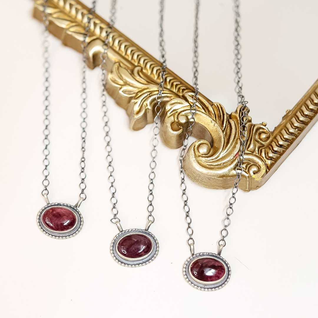 Three handmade Navajo necklaces with deep purple spiny oyster shell stones set in sterling silver with beaded edge detailing, displayed on a gold ornate frame.