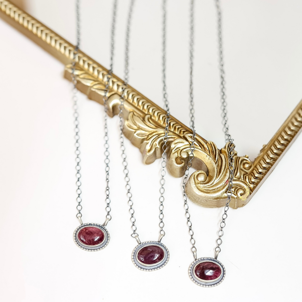 Three handmade Navajo necklaces with deep purple spiny oyster shell stones set in sterling silver with beaded edge detailing, displayed on a gold ornate frame.