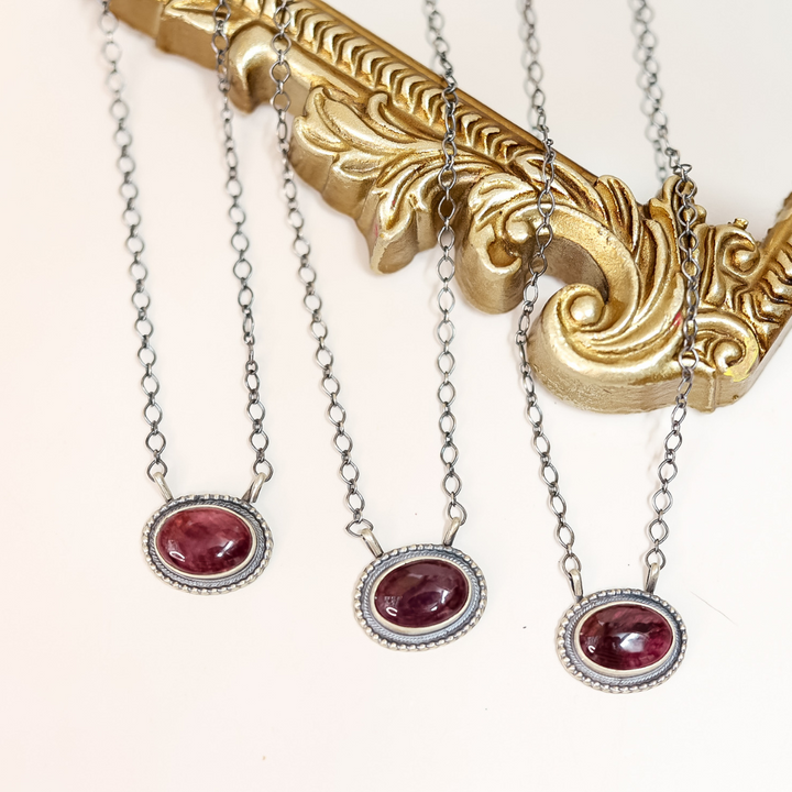 Three handmade Navajo necklaces with deep purple spiny oyster shell stones set in sterling silver with beaded edge detailing, displayed on a gold ornate frame.
