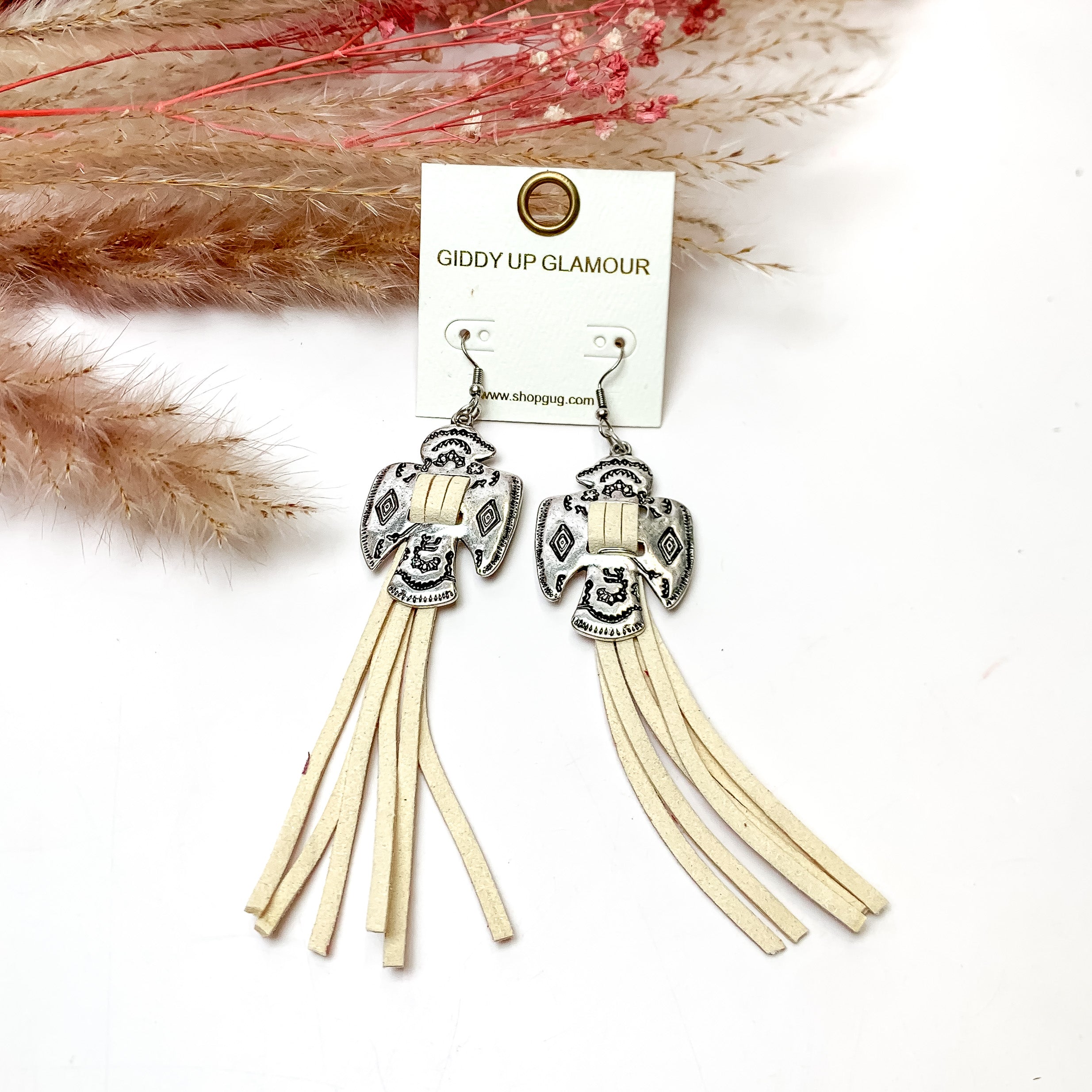Thunderbird Tassel Earrings in Ivory. These earrings are pictured on a white background with flowers behind for decoration.