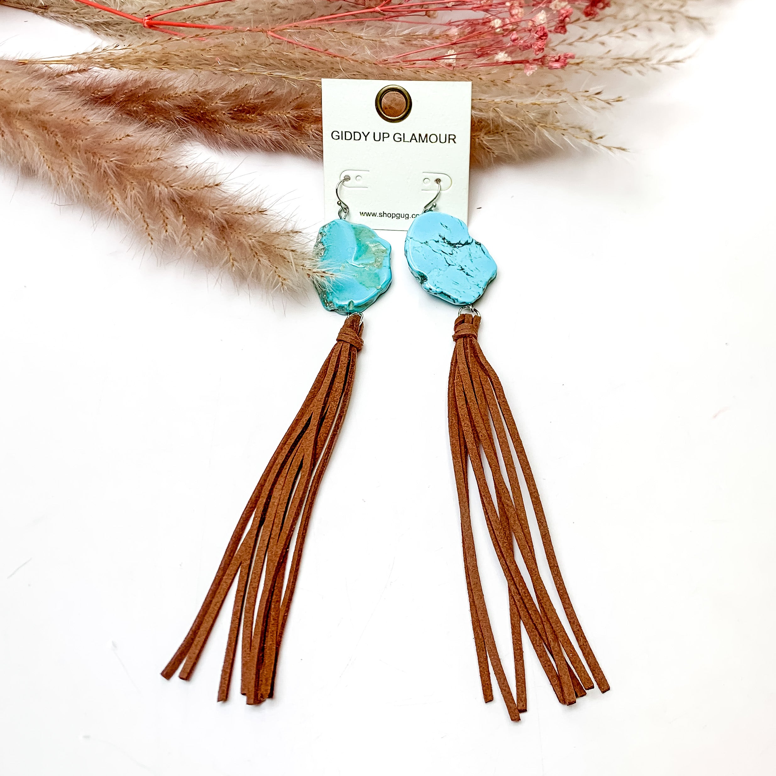 Turquoise Stone Tassel Earrings in Brown. These earrings are pictured on a white background with flowers behind for decoration.