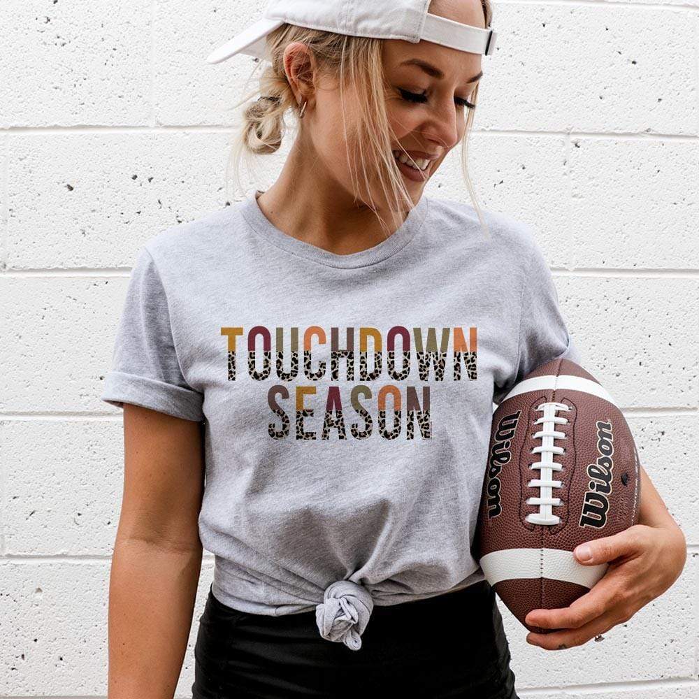 Model is wearing a gray short sleeve crewneck featuring a half multicolor half leopard print graphic that says "Touchdown season"