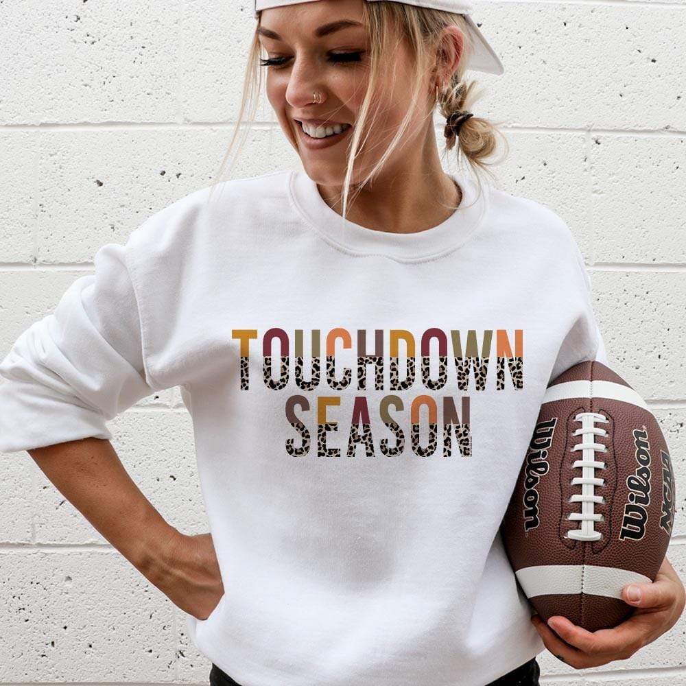 Model is wearing a white sweatshirt featuring a half multicolor half leopard print graphic that says "Touchdown season"