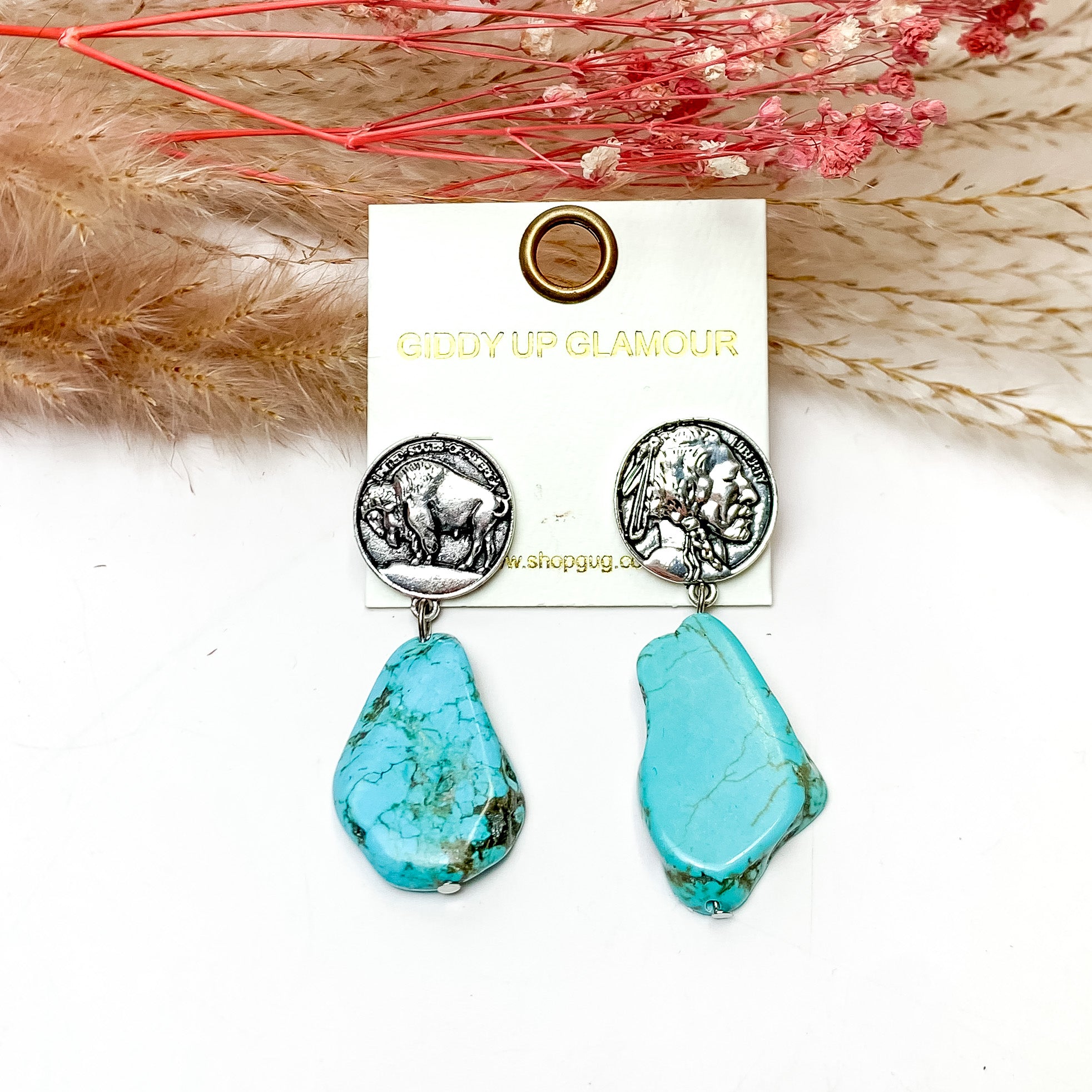 Turquoise Stone Earrings With Silver Tone Coin Posts. These earrings are pictured on a white background with flowers behind for decoration.