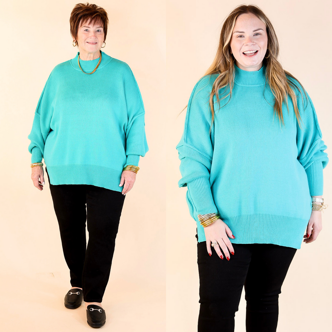 Models are wearing turquoise oversized sweater with side slit. One model is showcasing a smaller size while the other is wearing a larger size, both in combination with black pants and flat shoes.