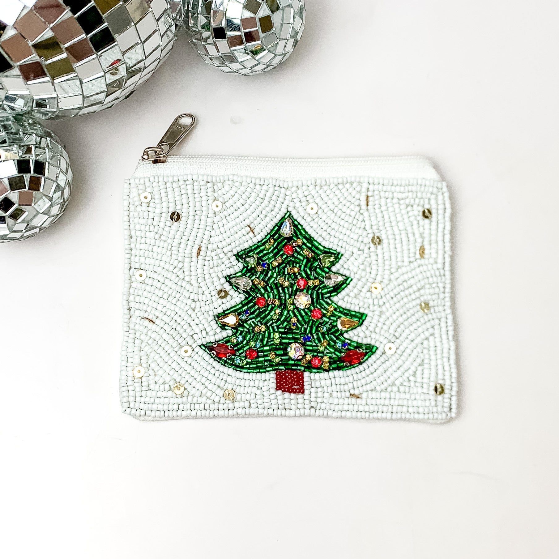 White beaded coin purse with a green Christmas tree and gold beads throughout. This coin purse is pictured on a white background with disco balls in the top left corner. 