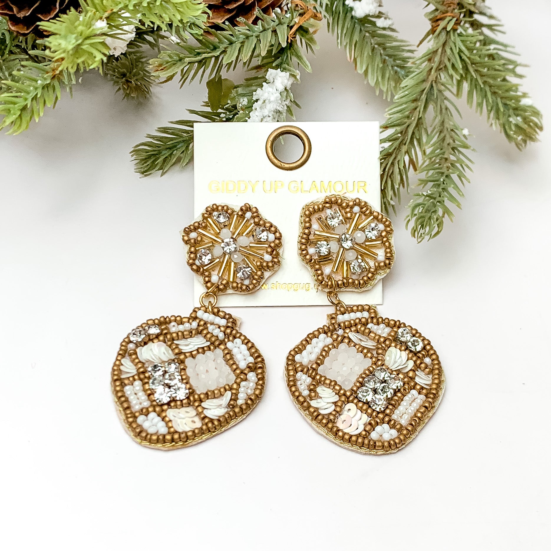 Ivory and gold beaded ornament shaped earrings. These earrings are pictured on a white background with pine trees at the top of the picture. 