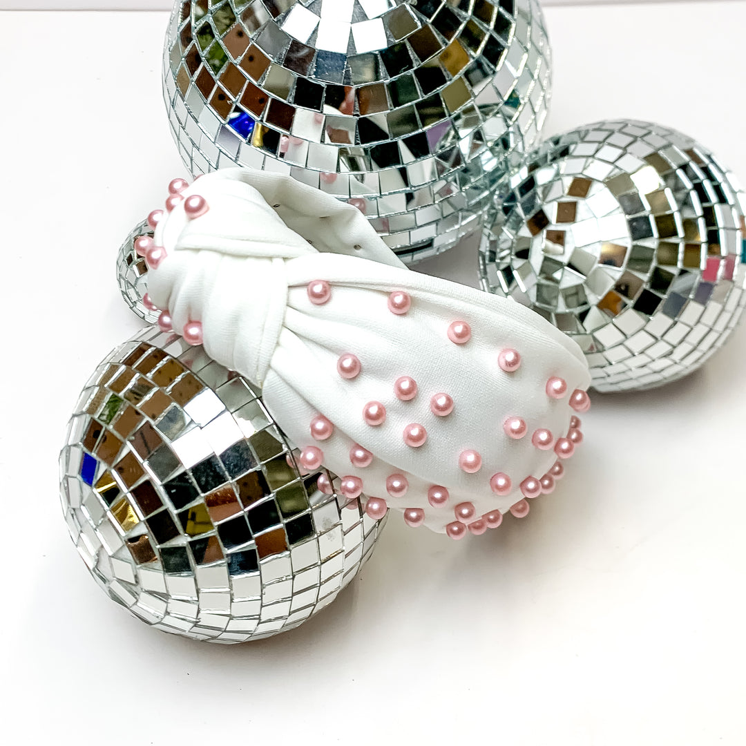 White Headband With Light Pink Pearls. This headband is pictured on a white background and is surrounded by disco balls.