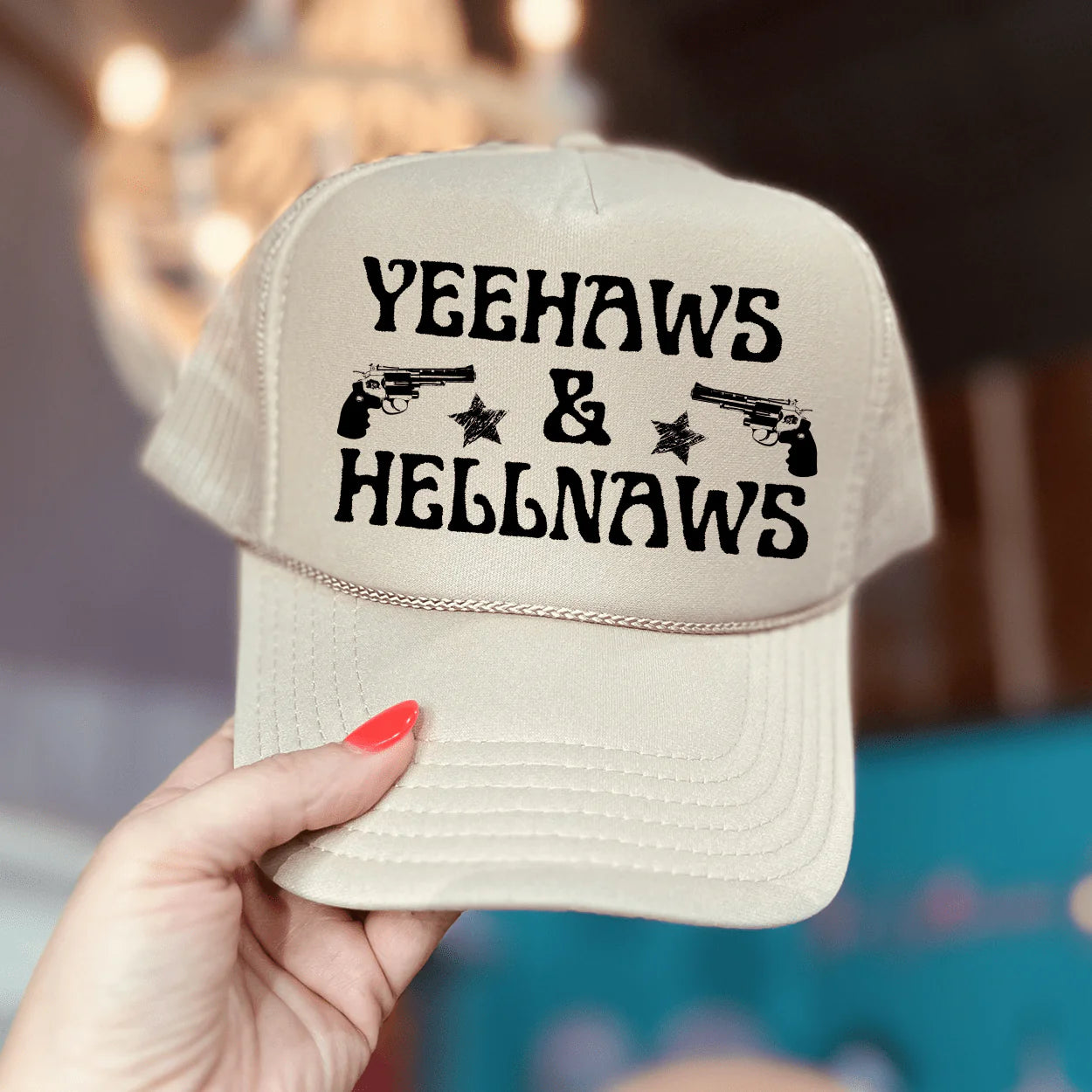 In the picture is a cream trucker hat that says yeehaws and hellnaws with stars on each side.