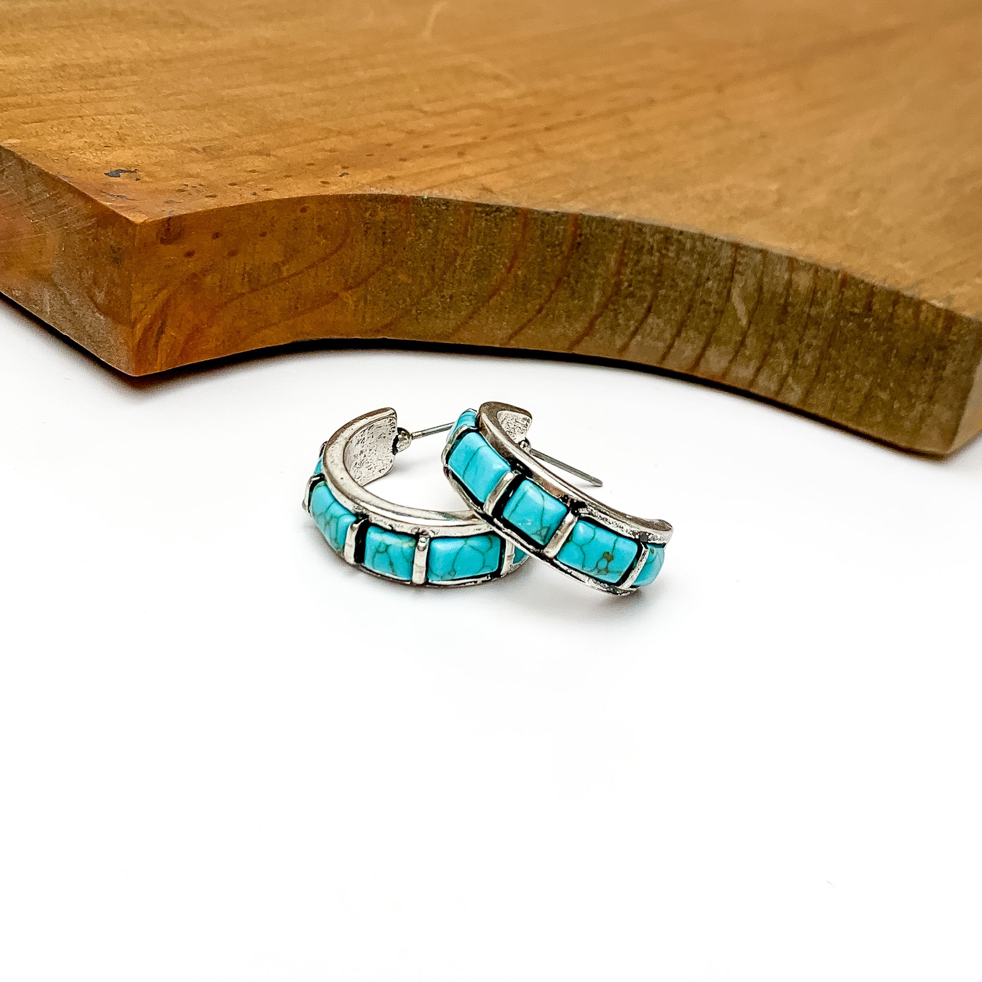 Turquois and silver tone medium size hoops earrings. Pictured with a white background and wood at the top.