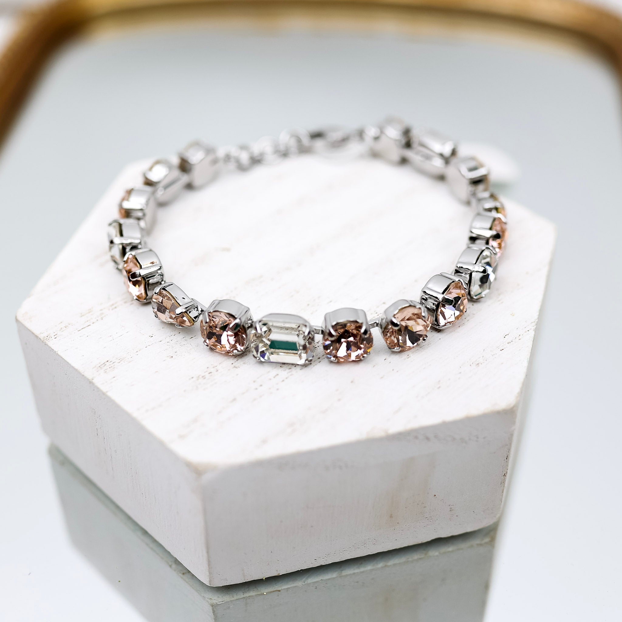 A silver tone tennis bracelet with cushion cut, emerald cut, and teardrop cut crystals that are topaz, blush, and clear.