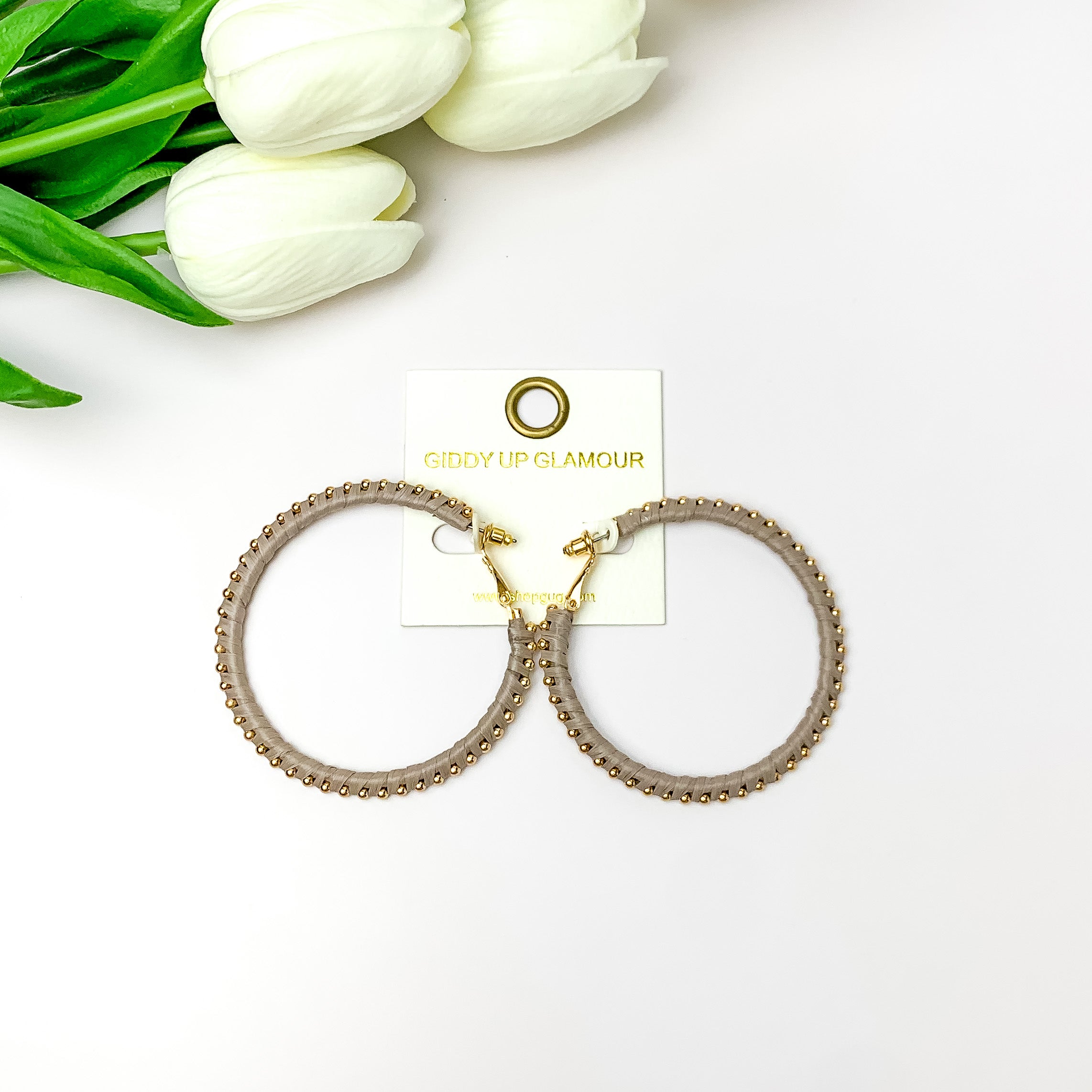Pictured are circle grey hoop earrings with gold beads around it. They are pictured with white flowers on a white background