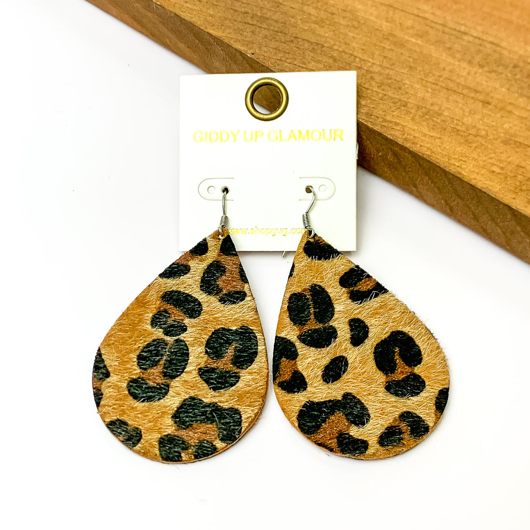 Large leopard print drop earrings.Pictured on a white background with a wood piece in the top right corner.