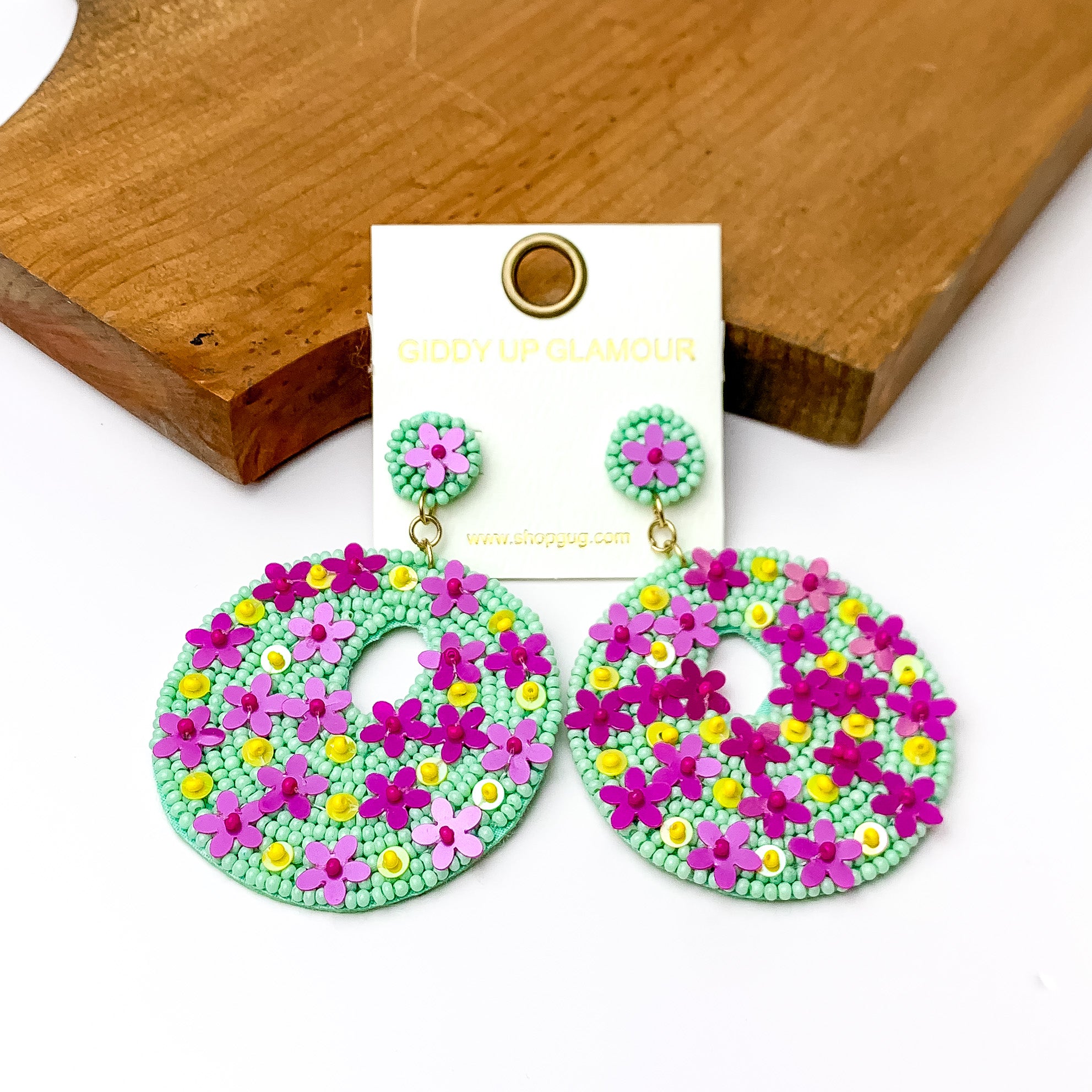 Mint green Beaded Circular Drop Earrings with Floral Designs. Pictured on a white background with a wood piece at the top. 
