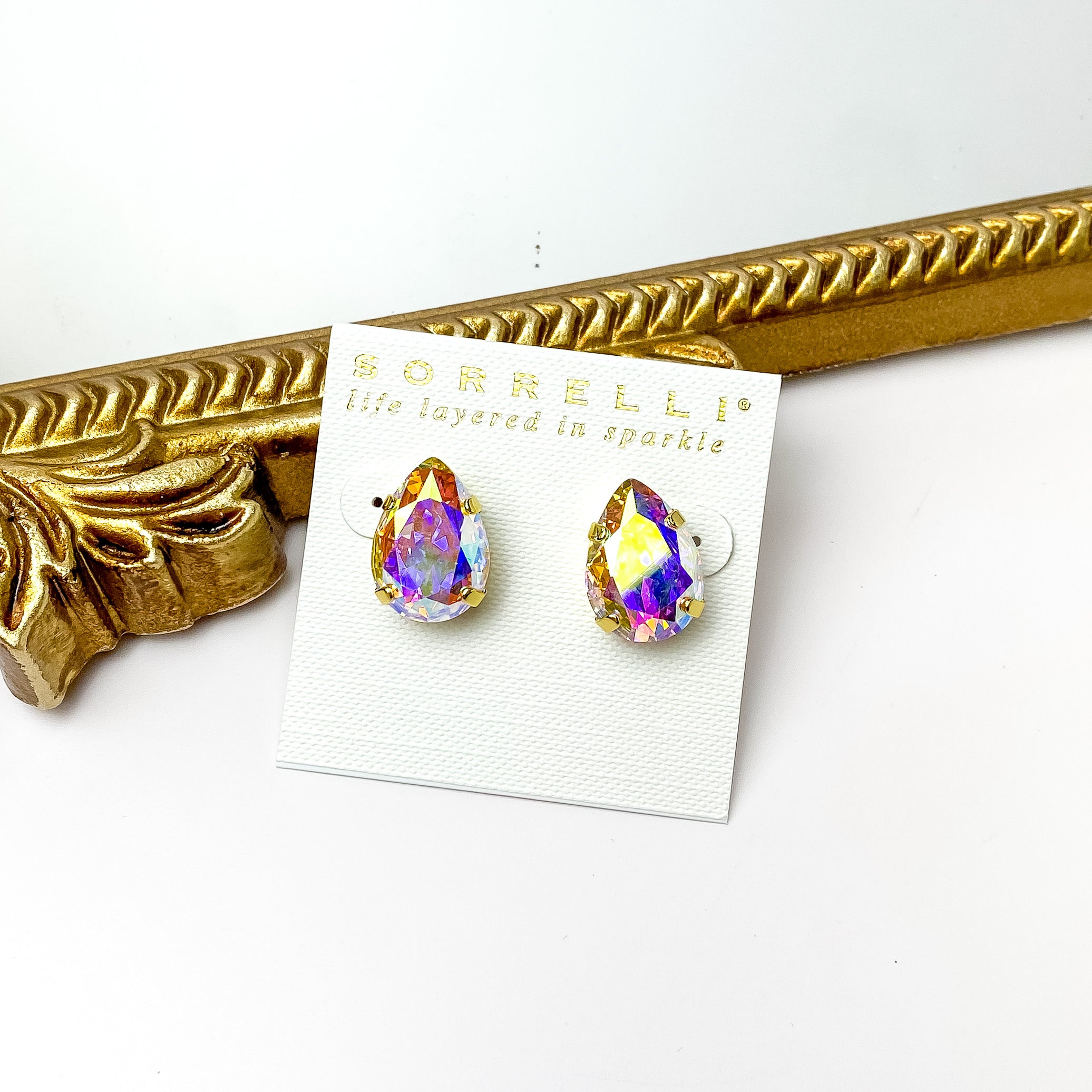 Single clear crystal stud earrings with a gold backing. Pictured on a white background with a gold figure through the middle