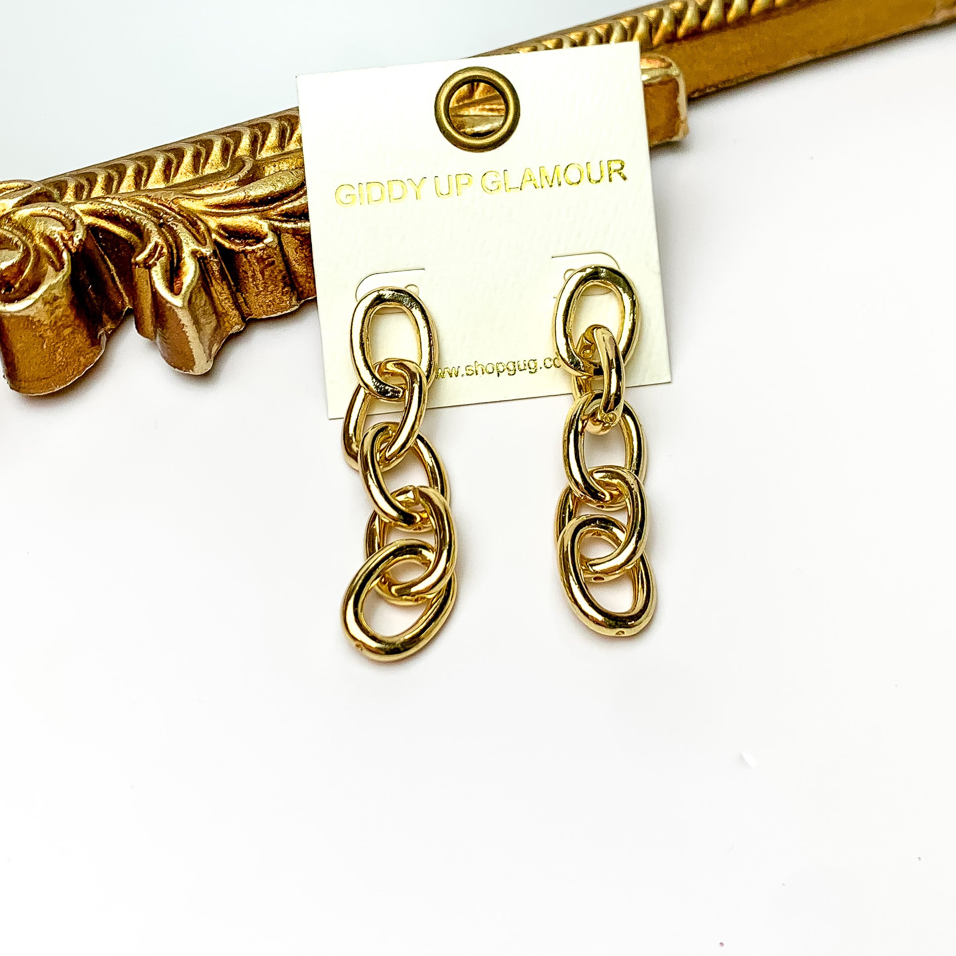 Gold tone chain dangle earrings. Pictured on a white background with a gold frame through it