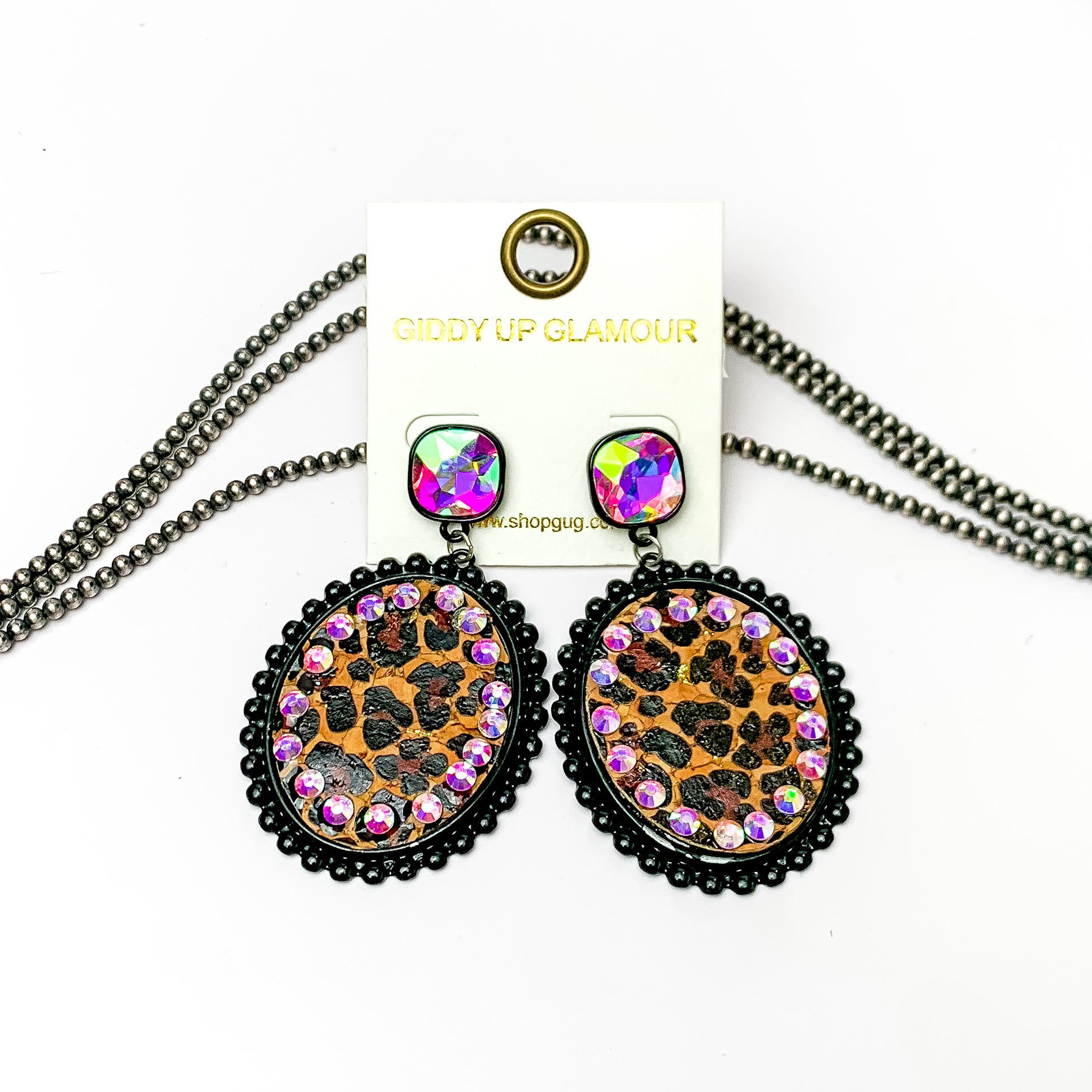 These earrings are oval shaped with leopard print inlay with the outline of the earing is black but also has ab crystal going around the oval shape. These pair of earrings also have a ab crystal post style earring. Pictured on a white background with navajo pearls behind it.