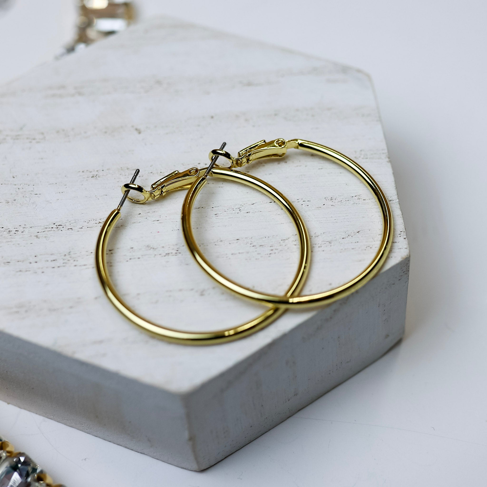 A pair of gold-tone circle hoop earrings pictured on a white background with crystal necklaces.