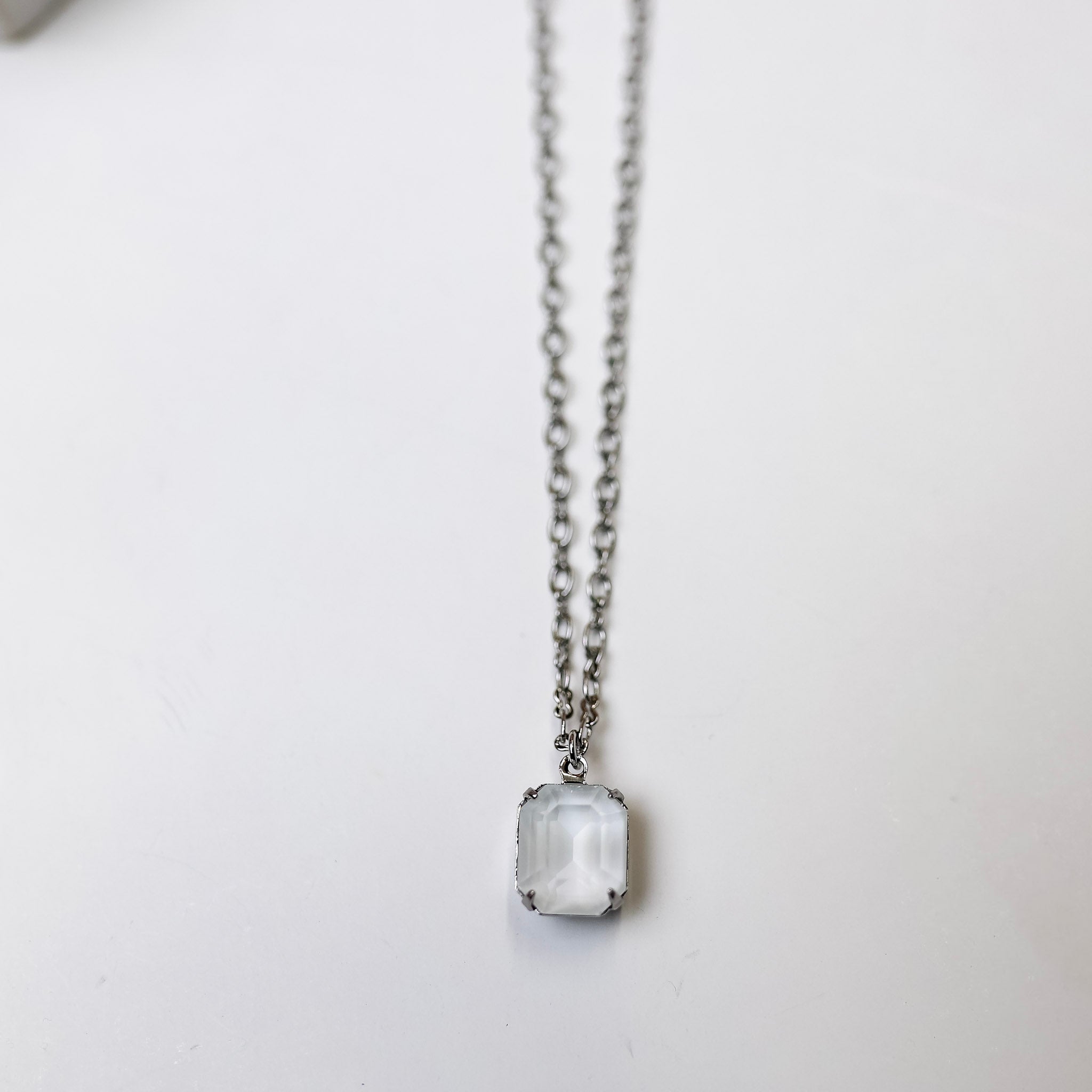 A silver tone chain necklace with an ivory emerald cut crystal pendant.