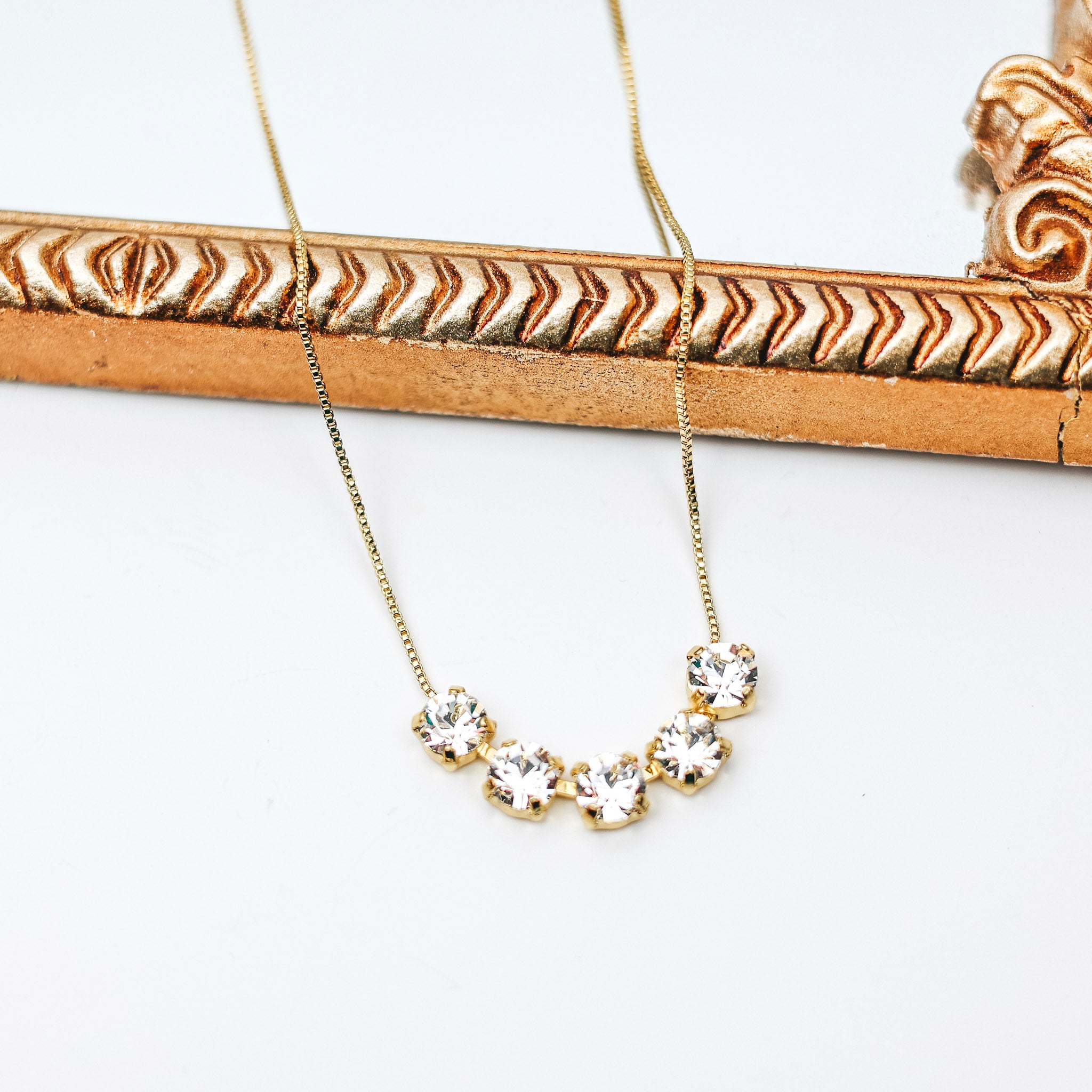 A gold chain necklace necklace with 4 clear crystals at the center. Pictured on a white background with a mirror.
