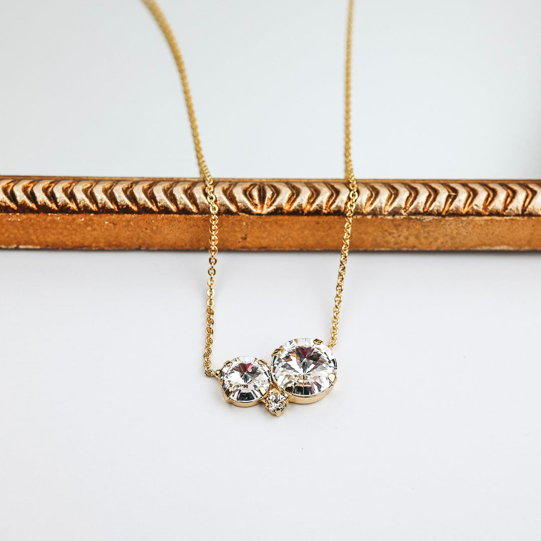 This necklace has a gold-tone chain with two circle crystals at the center. This necklace is pictured on a white background with a mirror.