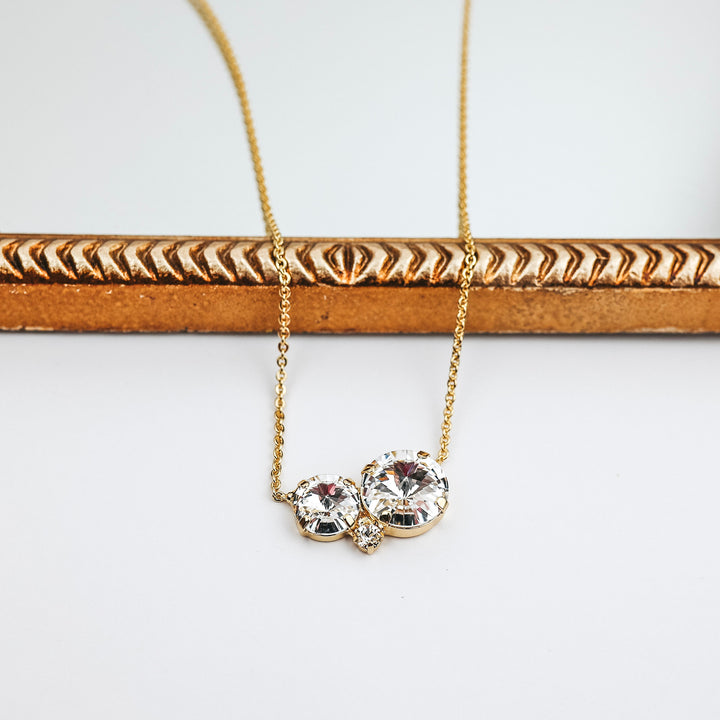 This necklace has a gold-tone chain with two circle crystals at the center. This necklace is pictured on a white background with a mirror.