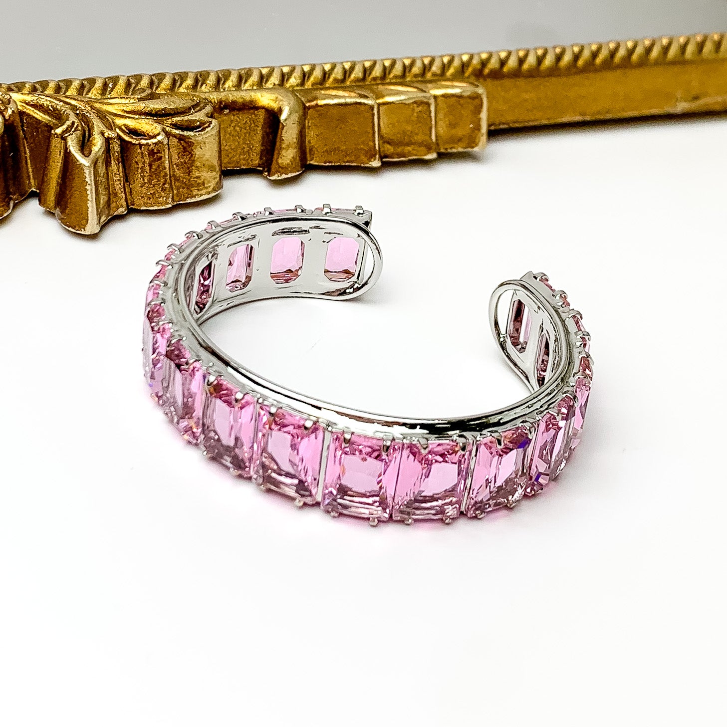 Silver bangle with a pink, rectangle crystal inlay. This bracelet is pictured on a white background with a gold mirror at the top of the picture.  