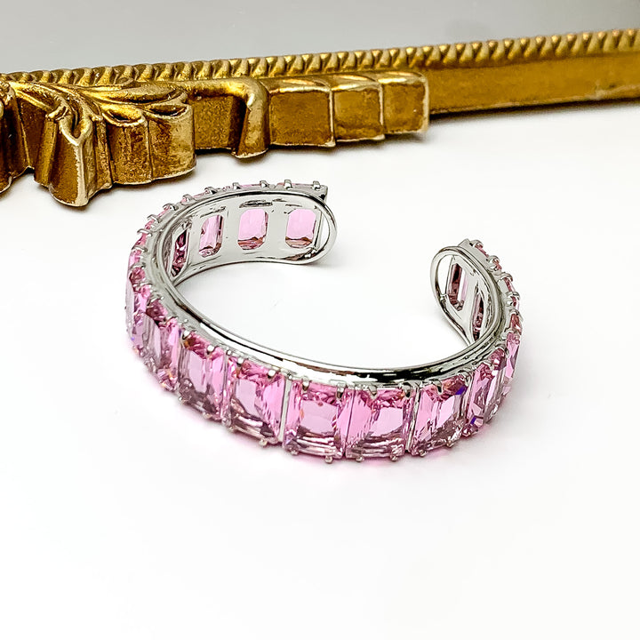 Silver bangle with a pink, rectangle crystal inlay. This bracelet is pictured on a white background with a gold mirror at the top of the picture.  