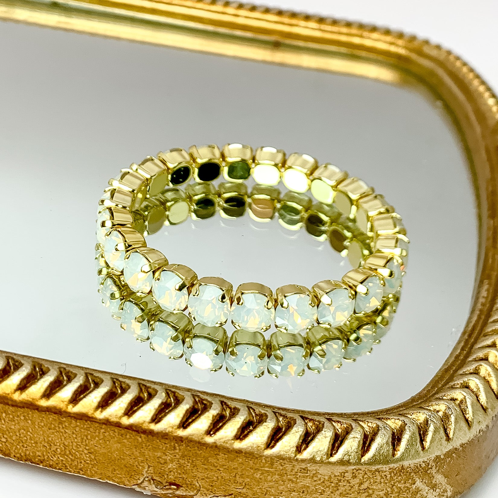 Stretchy white opal crystal bracelet with gold undertones. Pictured on a mirror with a gold frame.