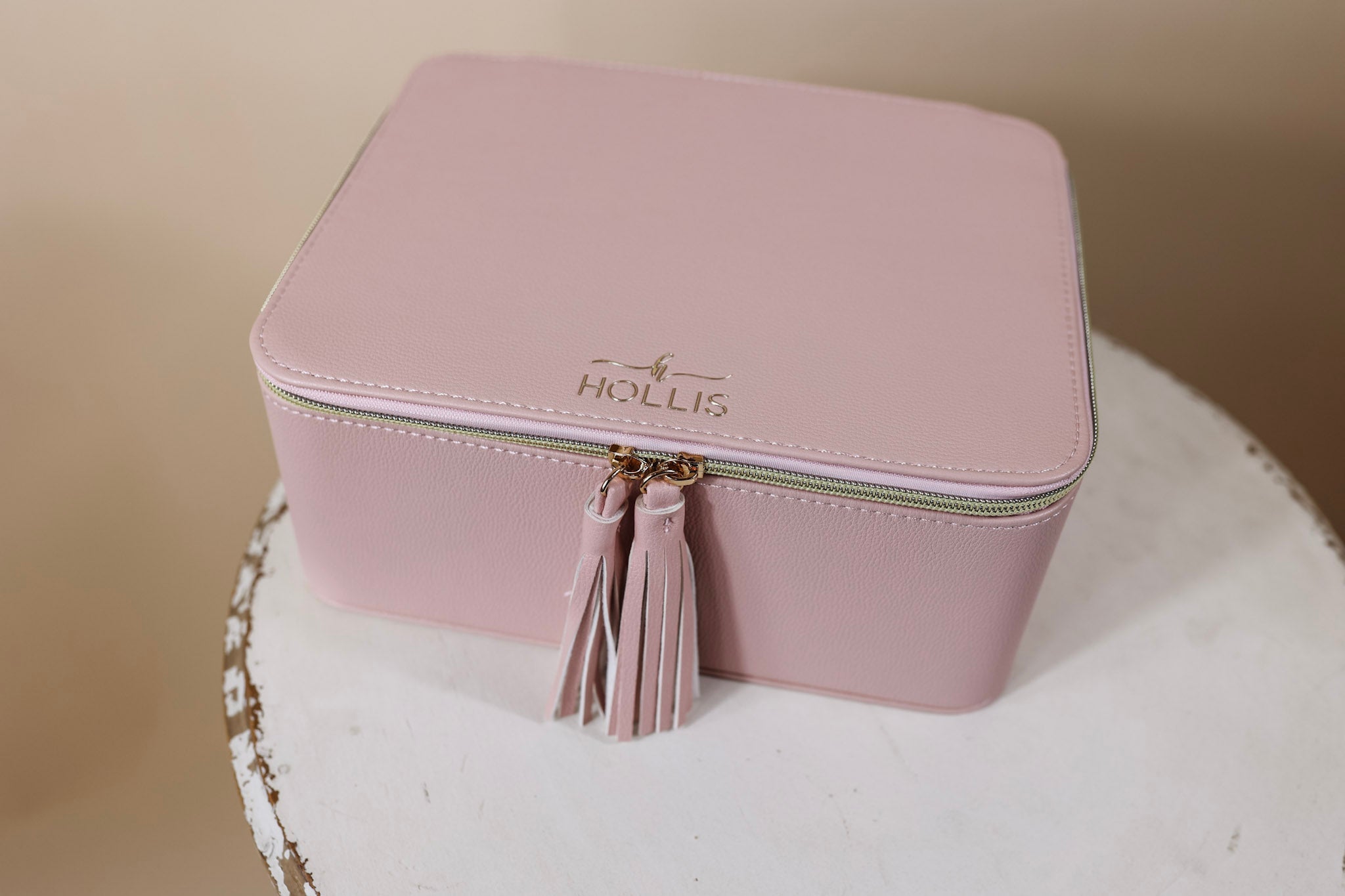 A blush pink bag is sitting in the middle of the picture. Background is solid tan. 