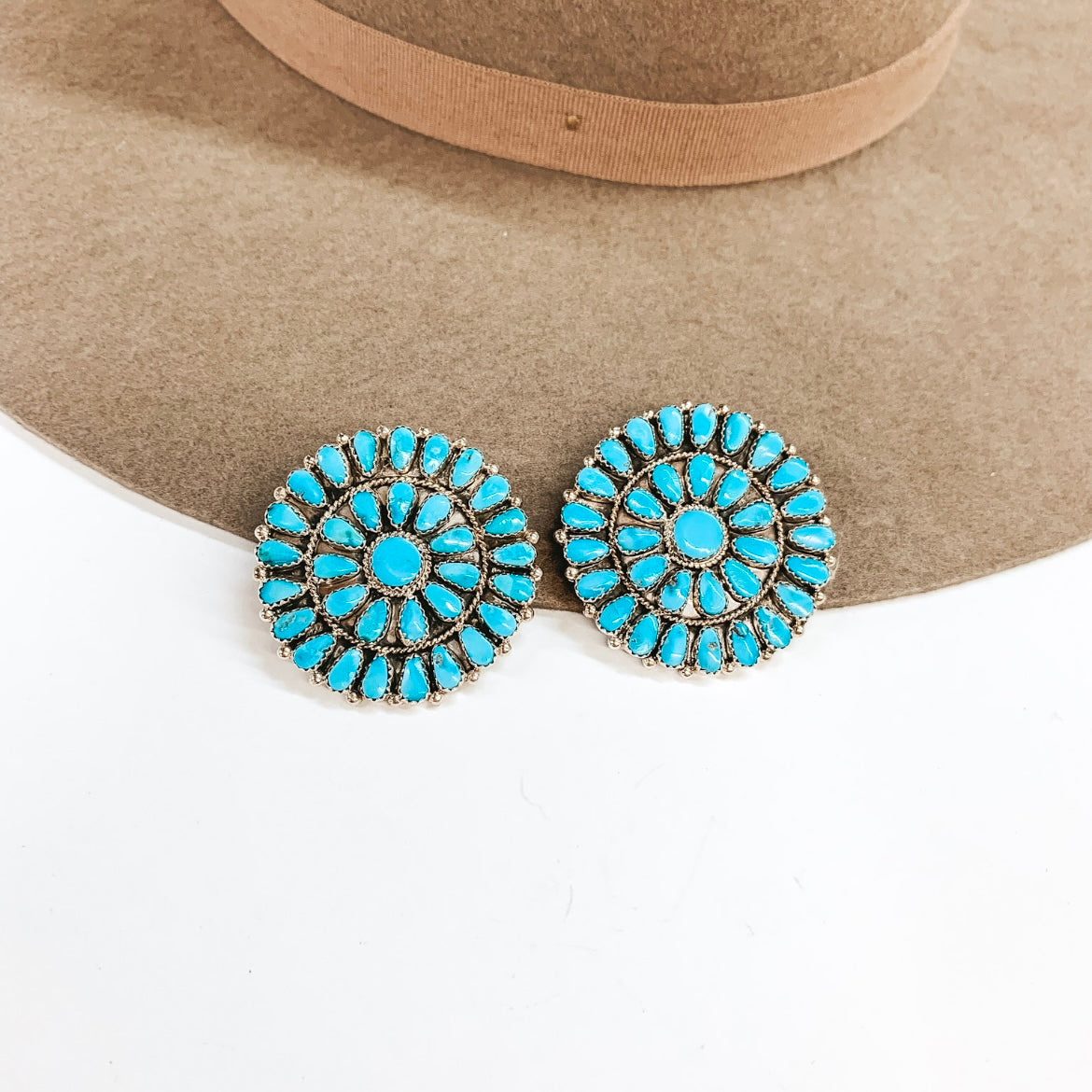 There is a pair of circle turquoise stone cluster earrings pictured with a hat on white background.