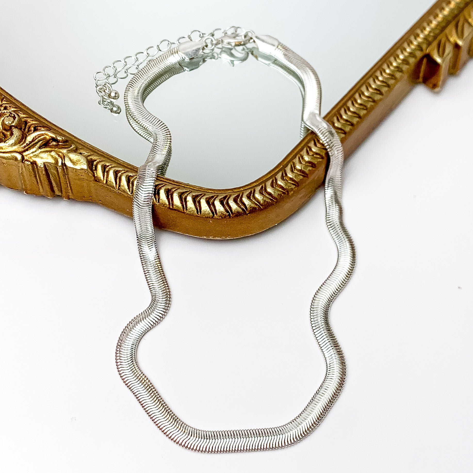 Silver tone classic chain necklace. Pictured on a white background with a gold frame through it.