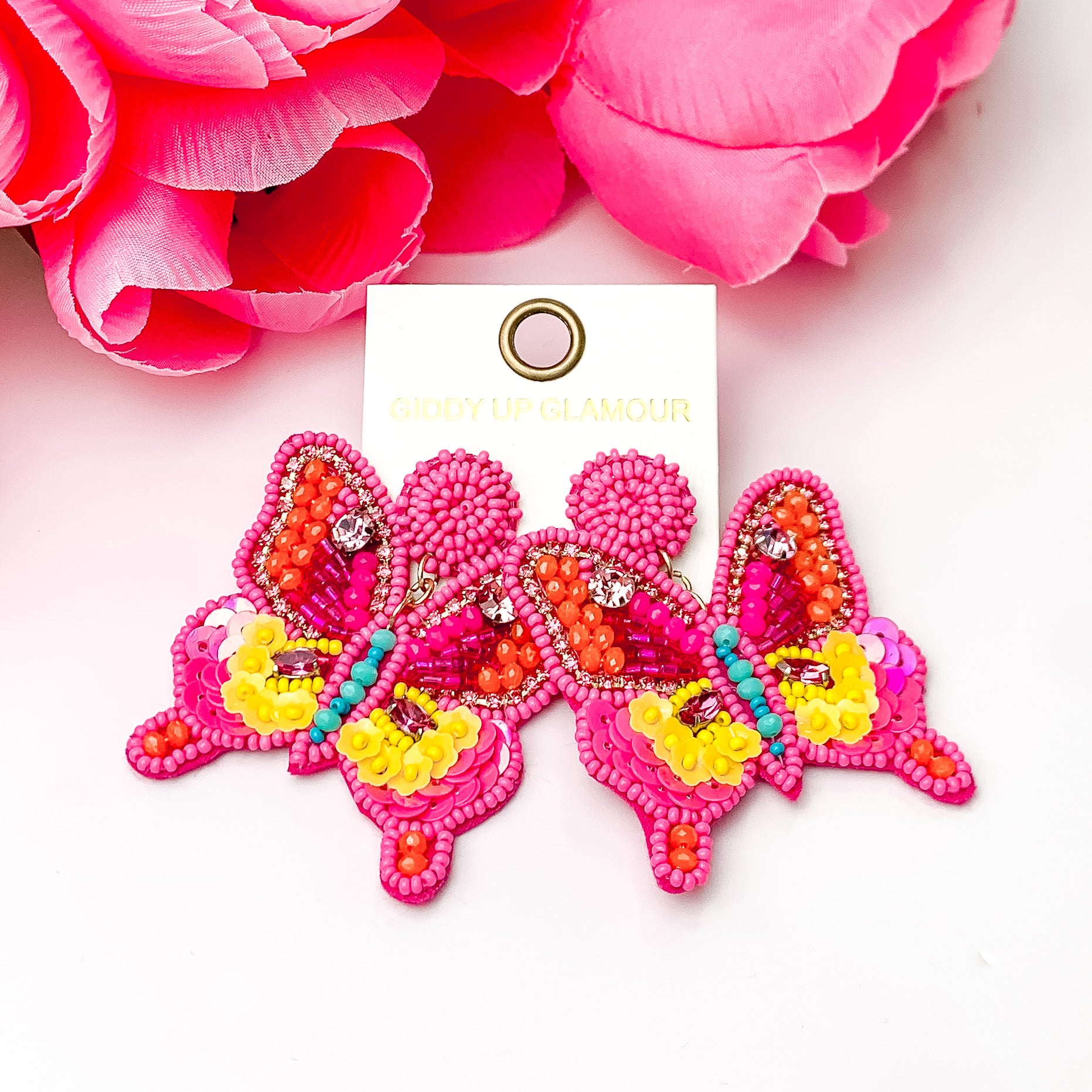 Hot Pink beaded butterfly earrings. Pictured on a white background with white flowers at the top.