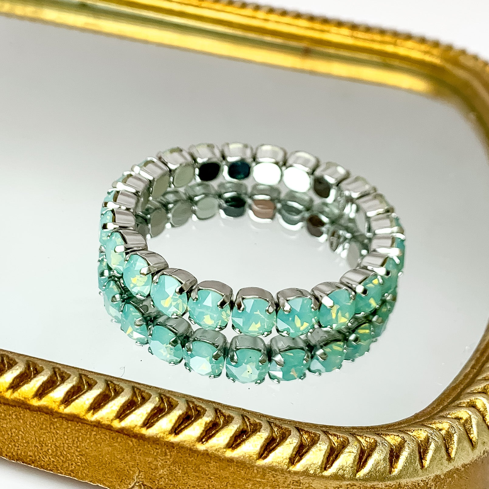 Single tier light blue crystal stretchy bracelt with silver undertones. Pictured on a mirror with a gold trim.