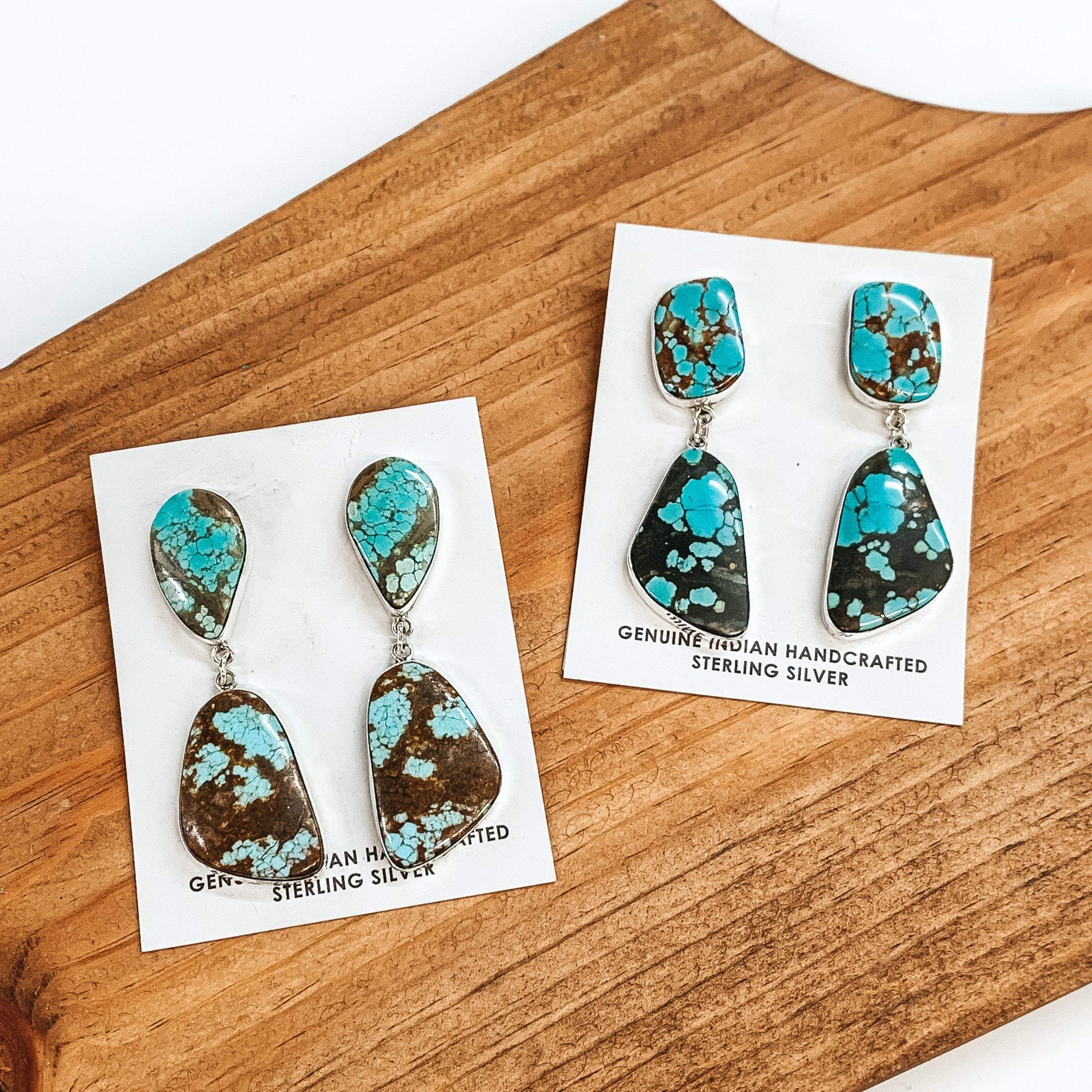 This picture includes two pairs on earrings with a silver backing, an irregular shaped post back earrings and an irregular shaped dangle. These earrings also include turquoise stones. These earrings are pictured on a brown block on a white background. 