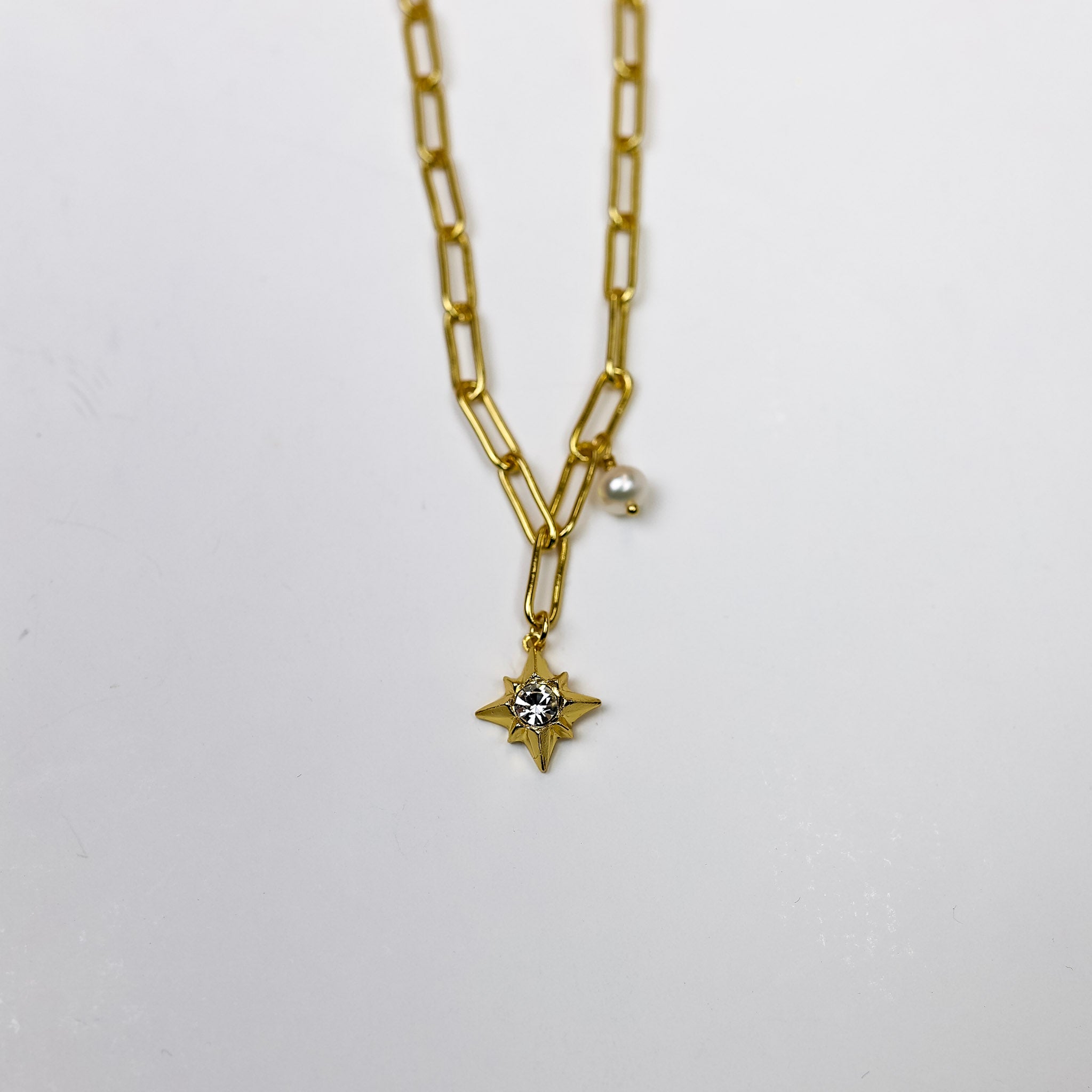 A gold-tone chain necklace with a small pearl pendant and star pendant with a crystal at the center.