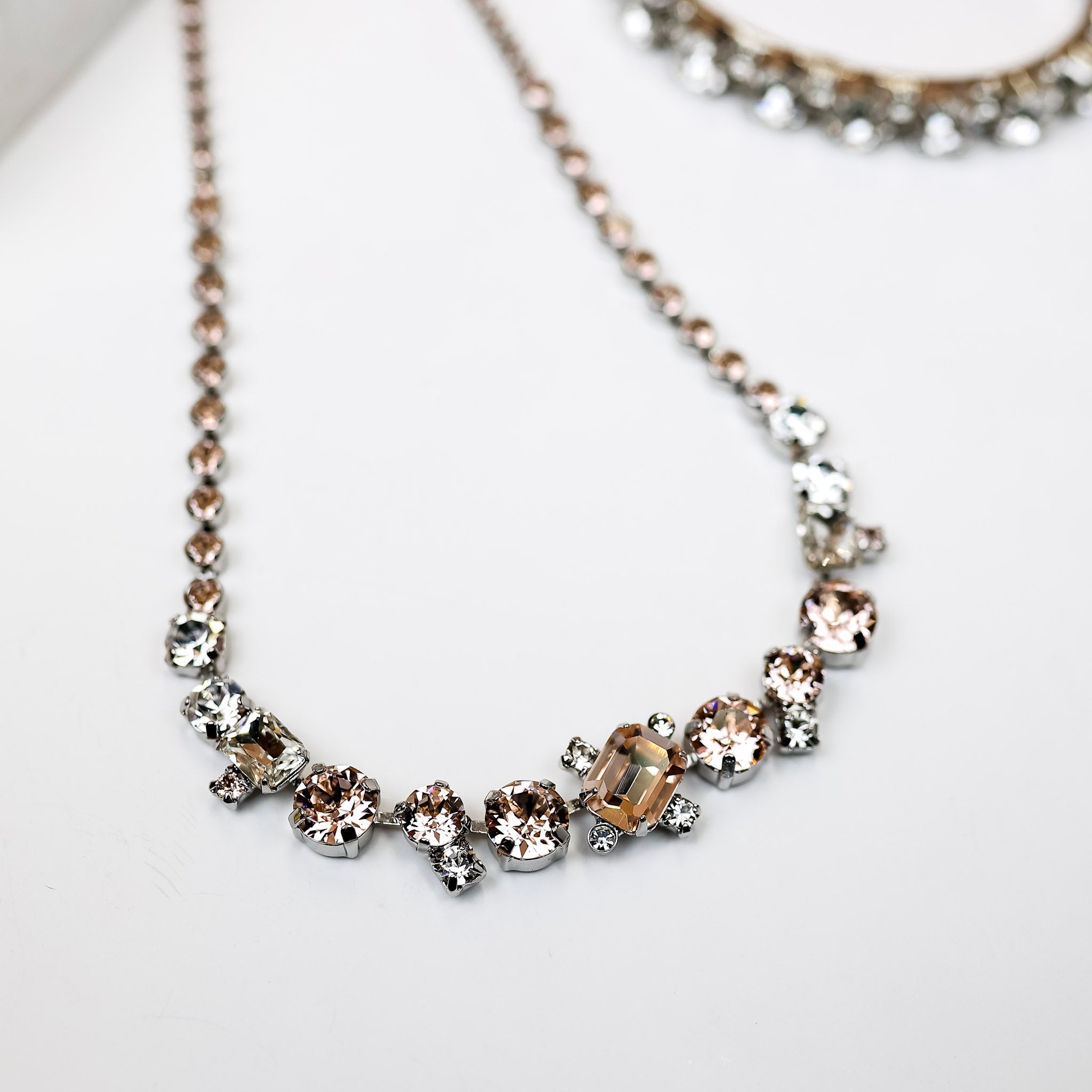 A necklace with blush and clear crystals along the entire chain with larger at the center.