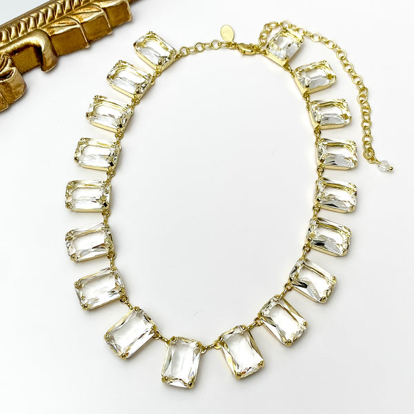 Clear rectangle crystal necklace. This necklace has a gold setting. This necklace is pictured on a white background with a gold mirror in the top left corner.   