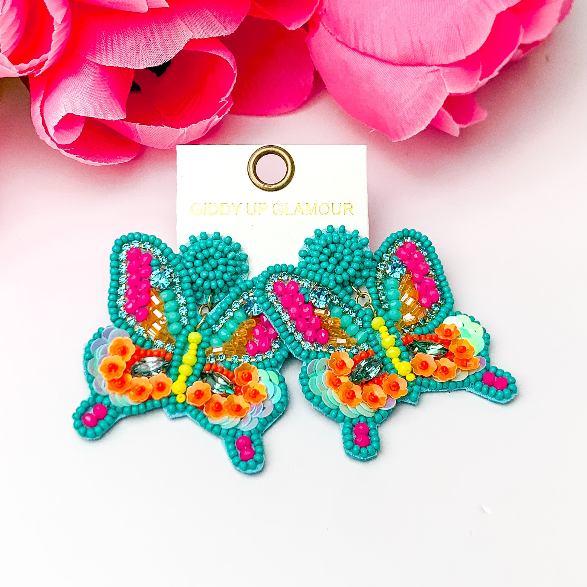 Beaded butterfly earrings in teal pink and orange. Pictured on a white background with pink flowers at the top.