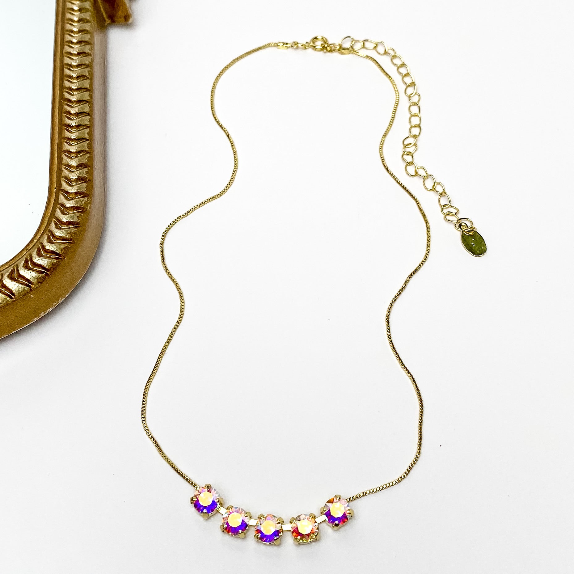 Pictured is a gold necklace with a five ab crystals. This necklace is pictured on a white background with a gold mirror on the left side.
