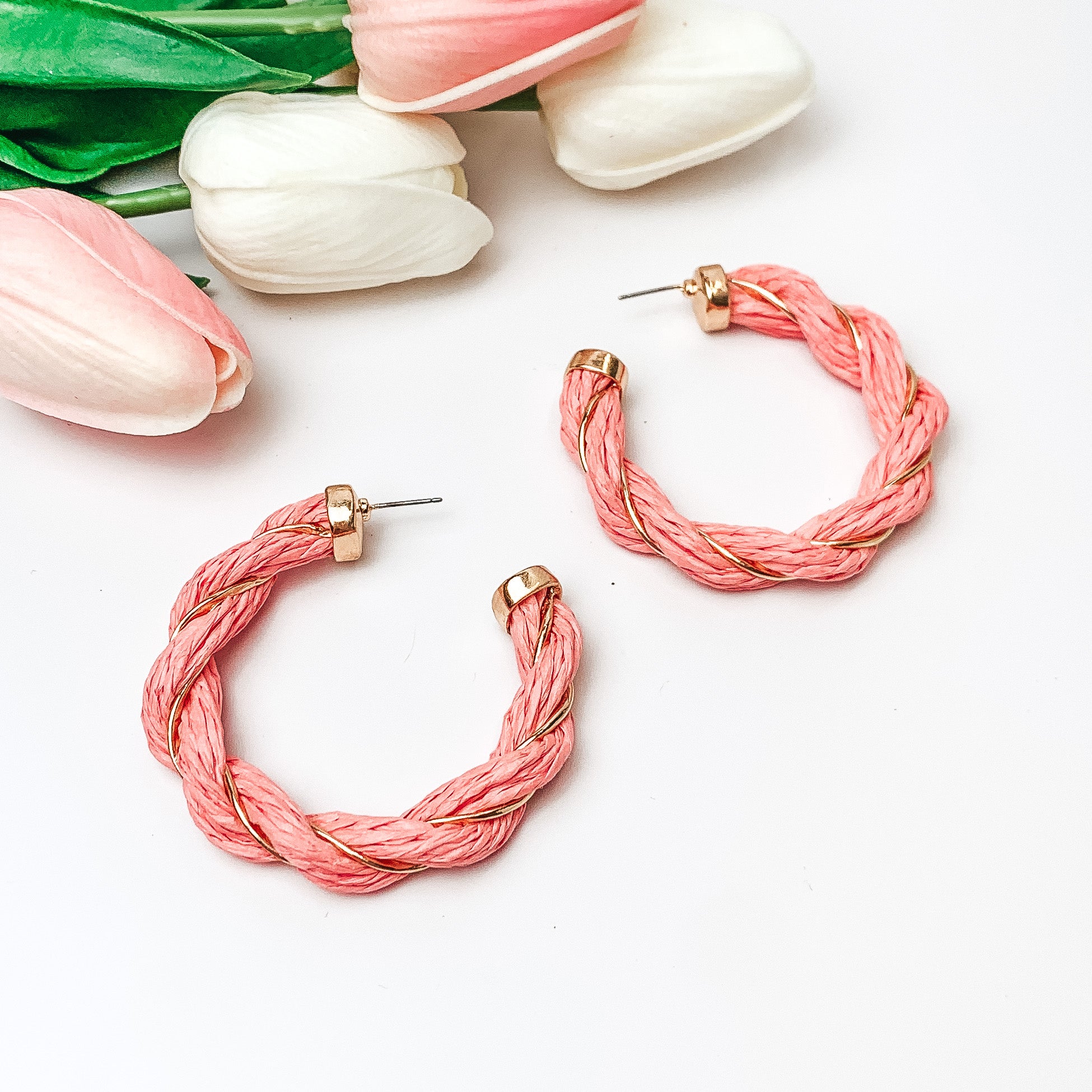 Pictured are pink raffia twisted hoop earrings with gold detailing.  They are pictured with pink and white tulips on a white background.