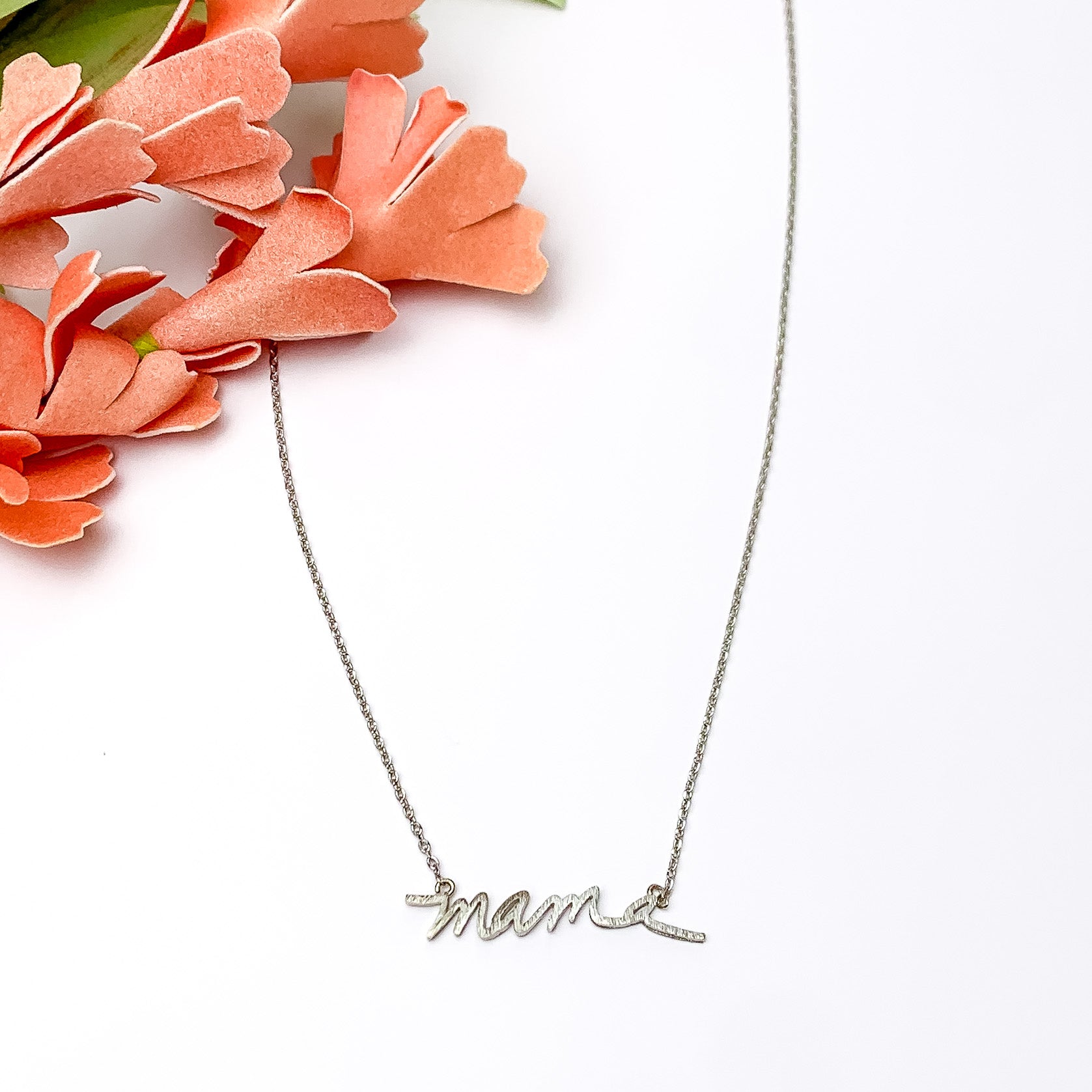 Mama chain necklace in silver tone. Pictured on a white background with flowers in the top left.