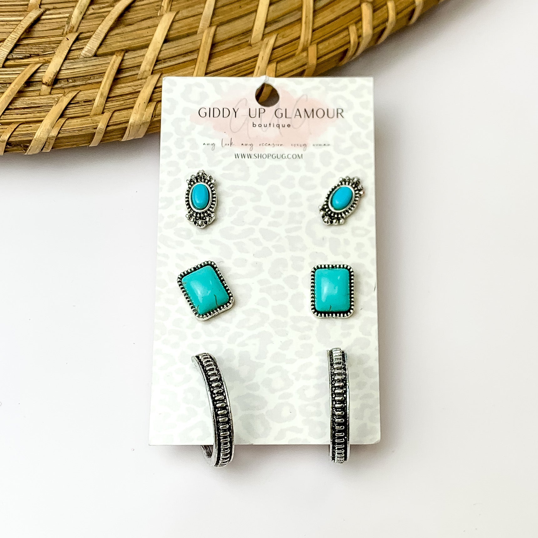 Pack of three turquoise and silver designed stud earrings. On a white background with wood like detail in the top left corner.