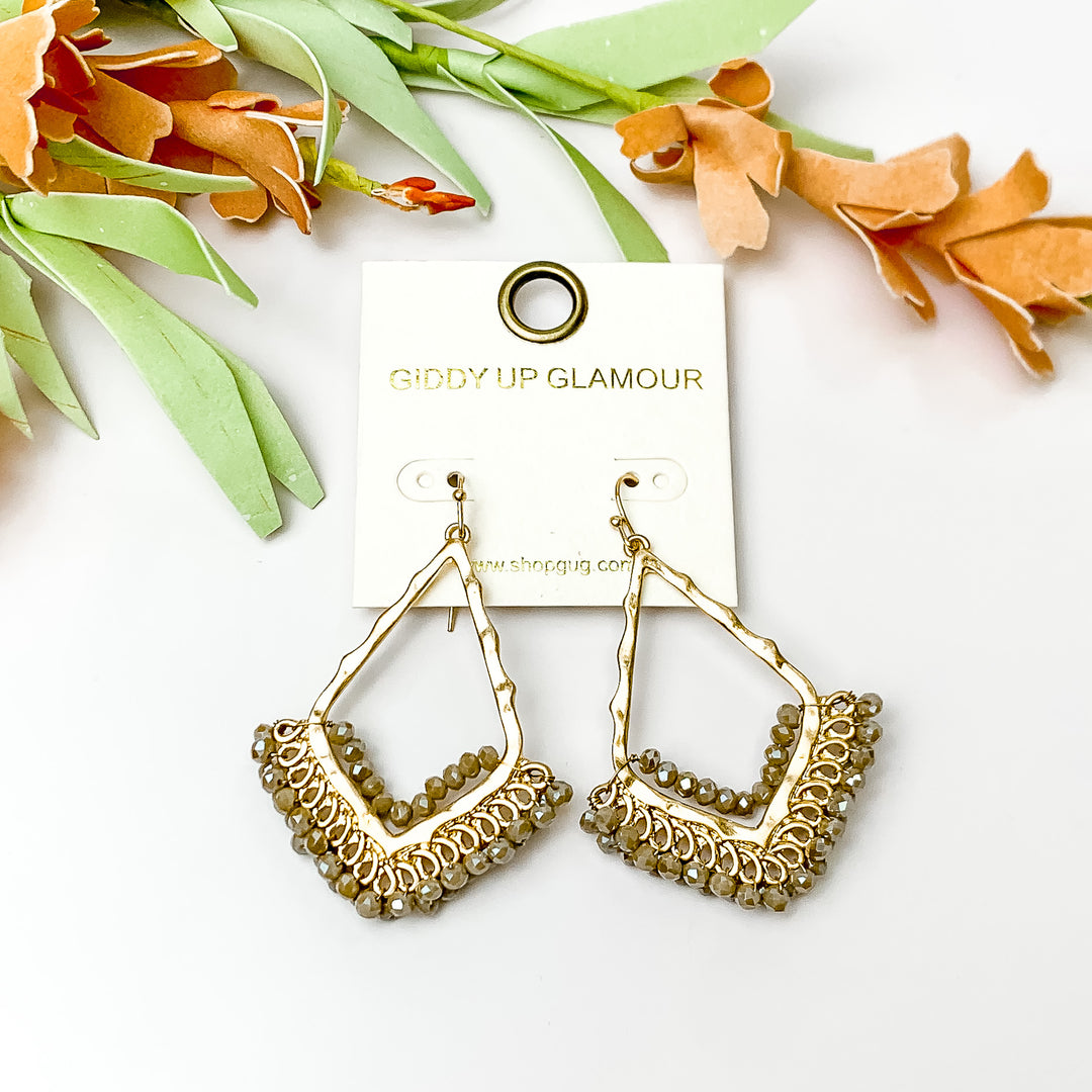 Beige crystal beads bordering open drop gold tone earrings. Pictured on a white background with flowers at the top.
