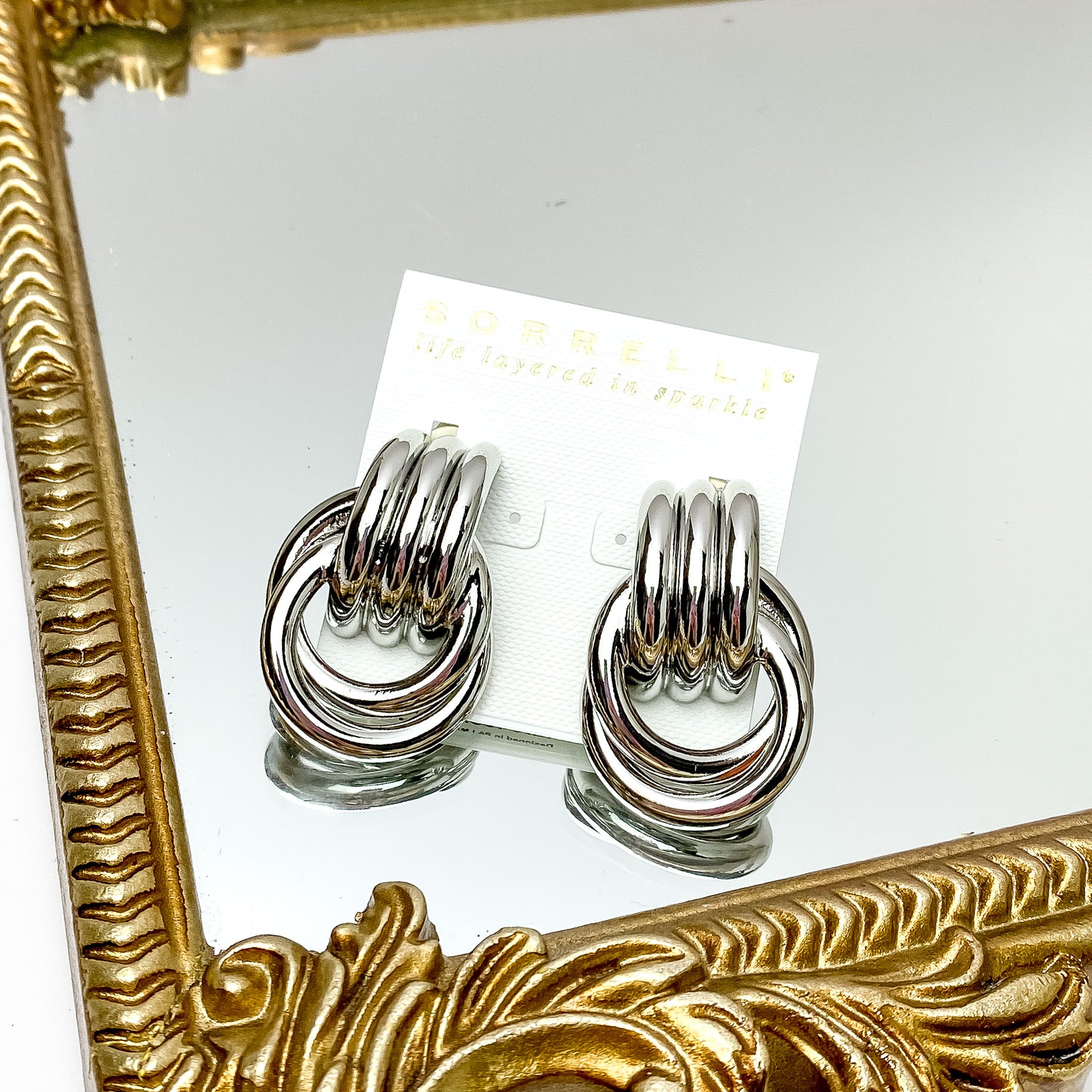 Two chunky silver earrings. These earrings feature links fused together and wrapped around eachother and pictured on a white cardstock. These earrings are pictured on a gold mirror on a white background. 