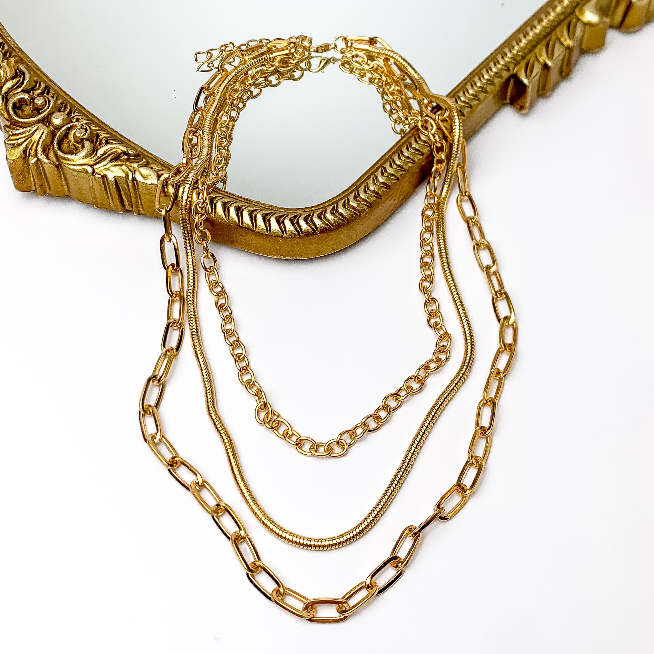 Set of three gold tone chain necklaces conneced. Pictured on a white background with a frame though it.