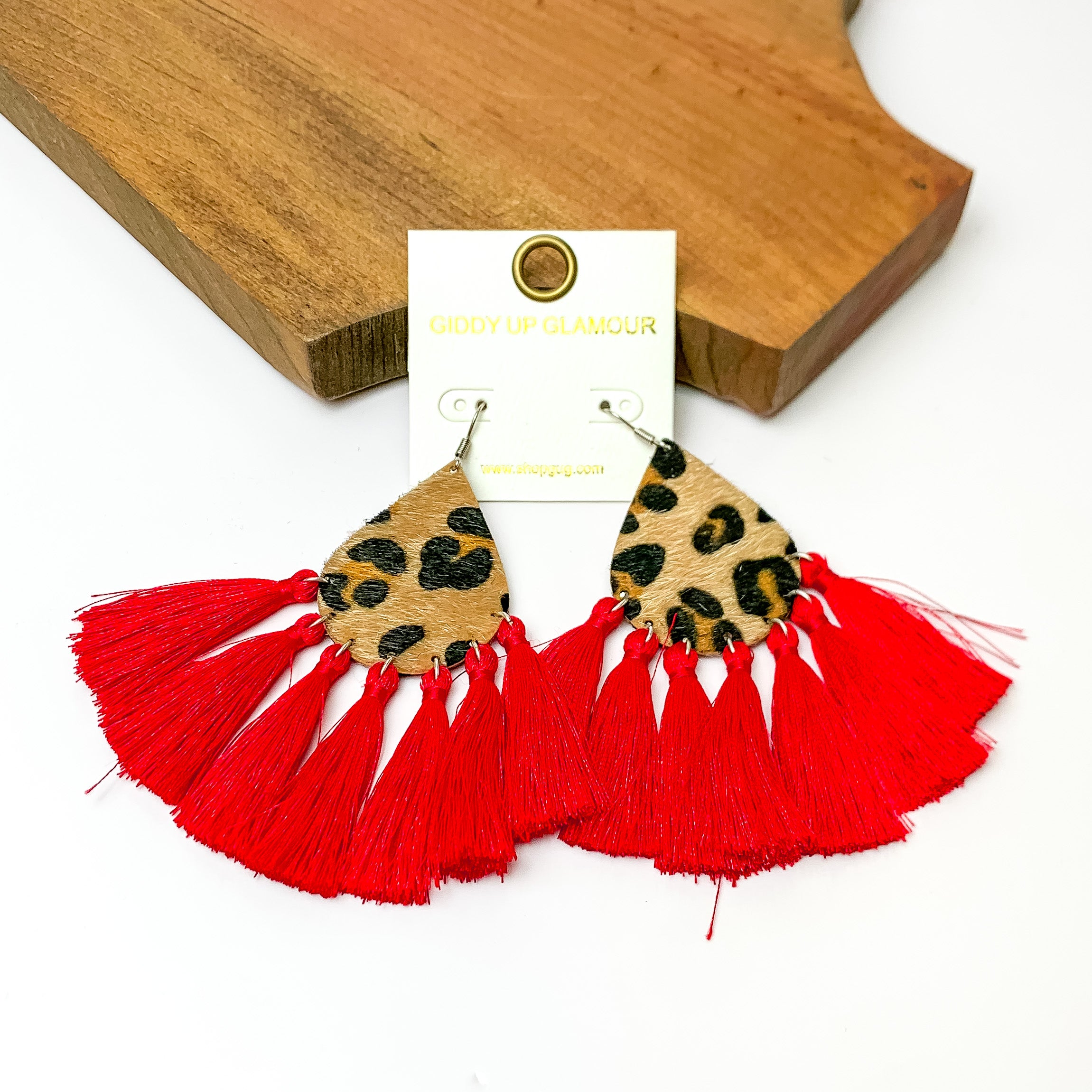 Leopard teardrop earrings with tassels trim in red. Pictured on a white background with a wood piece at the top.